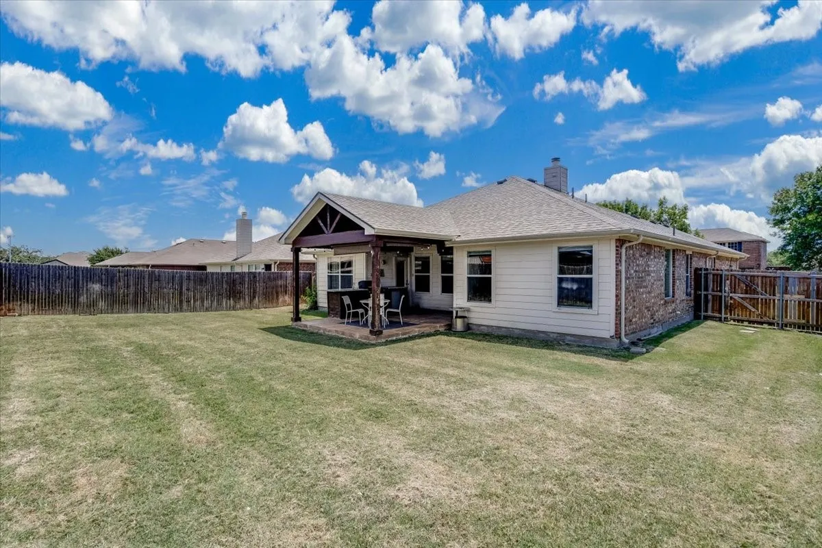 Spacious backyard featuring a covered patio, wood beam accents, brick siding, and a wooden privacy fence