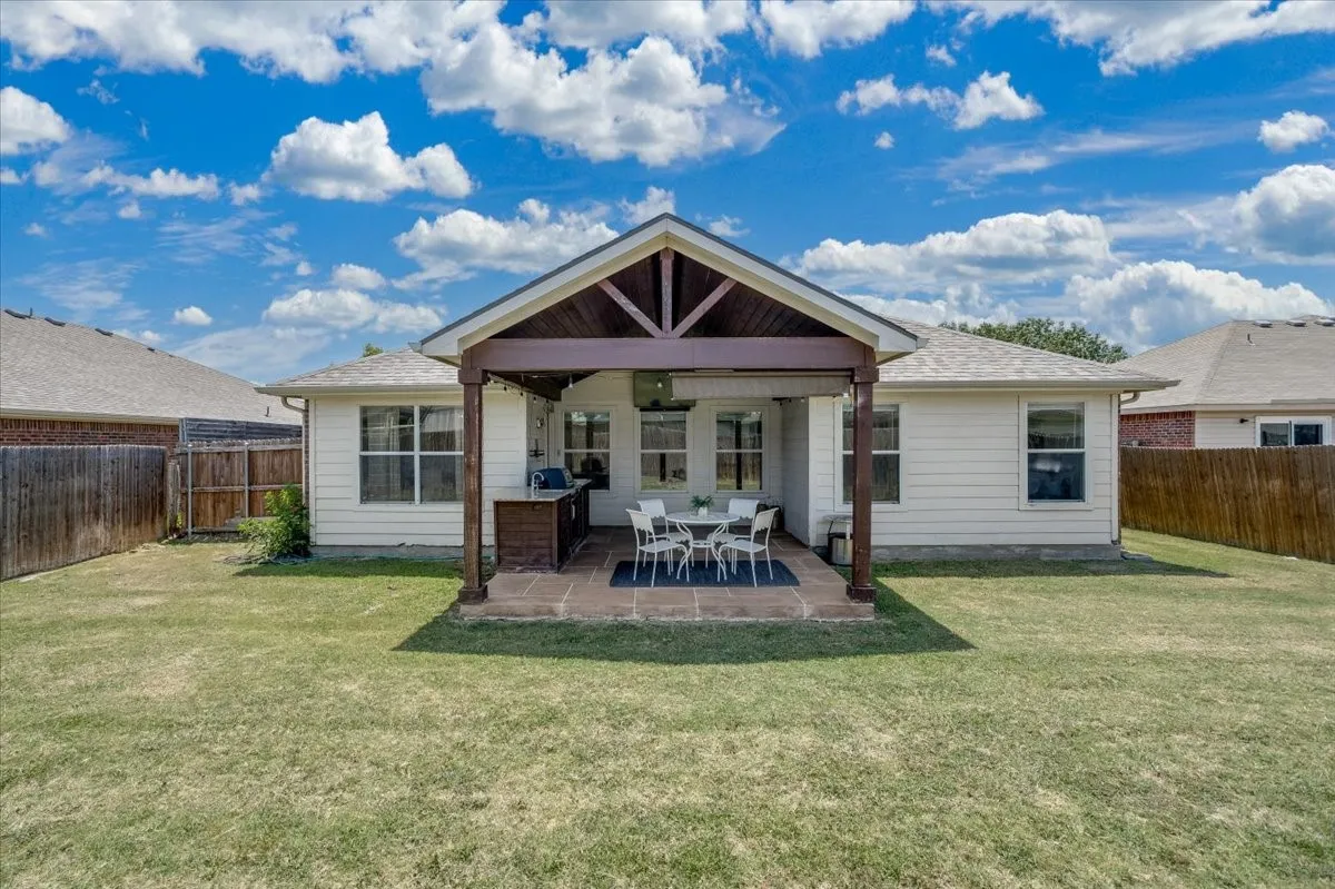 Expansive backyard featuring a covered patio, exposed beam roof structure, outdoor cooking station, and a level lawn