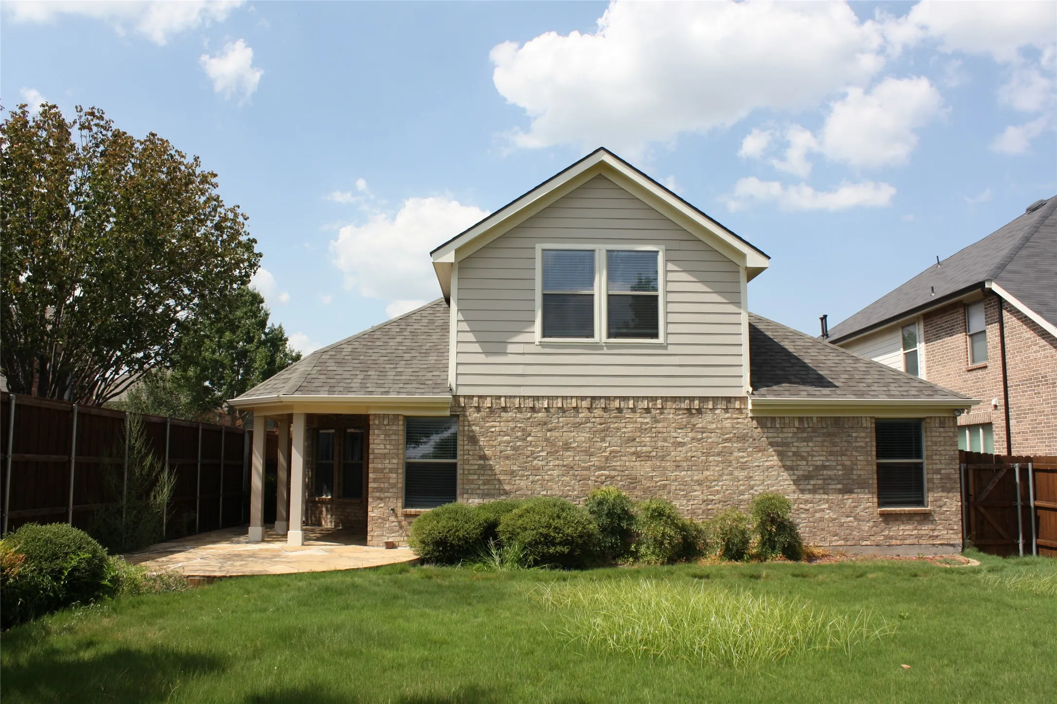 Brick and siding exterior with a covered patio, dual windows, and a shingled roof