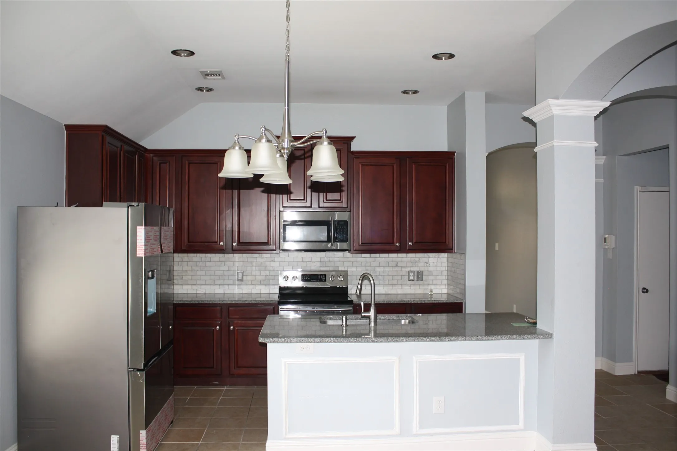 Kitchen featuring rich wood-finish cabinetry, stainless steel appliances, a tile backsplash, and a breakfast bar with a solid surface countertop