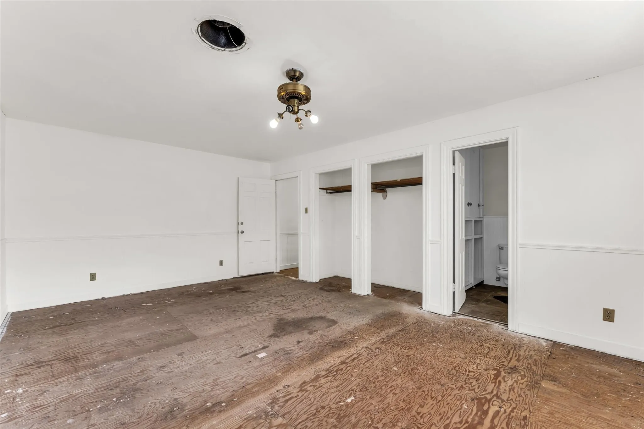 Upstairs at the end of the hallway, white walls with wainscoting, two open closet spaces, a built-in ceiling light fixture, and an interior door