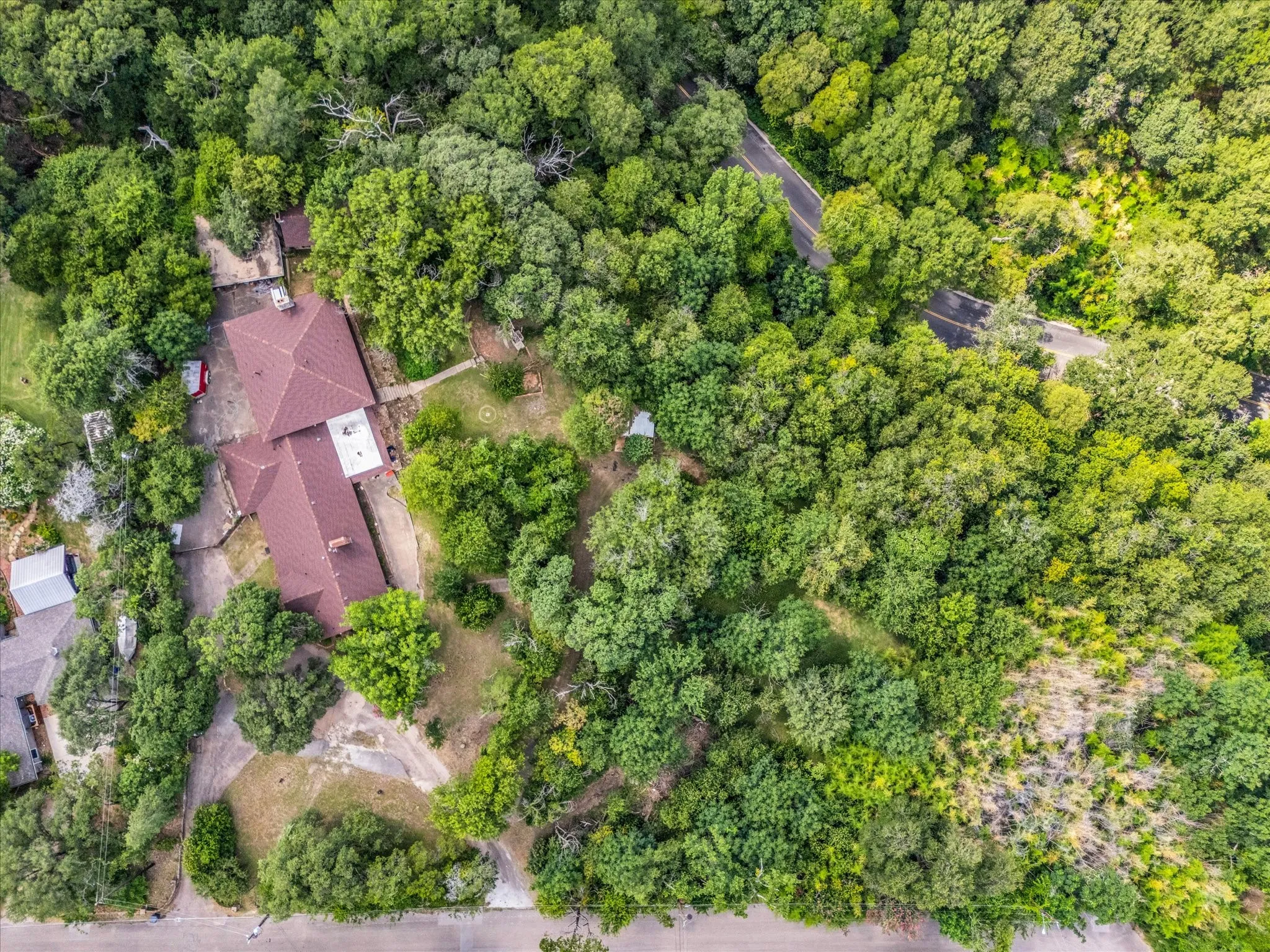 Expansive property featuring a brown shingle roof, surrounded by mature trees, with visible paved and unpaved driveways