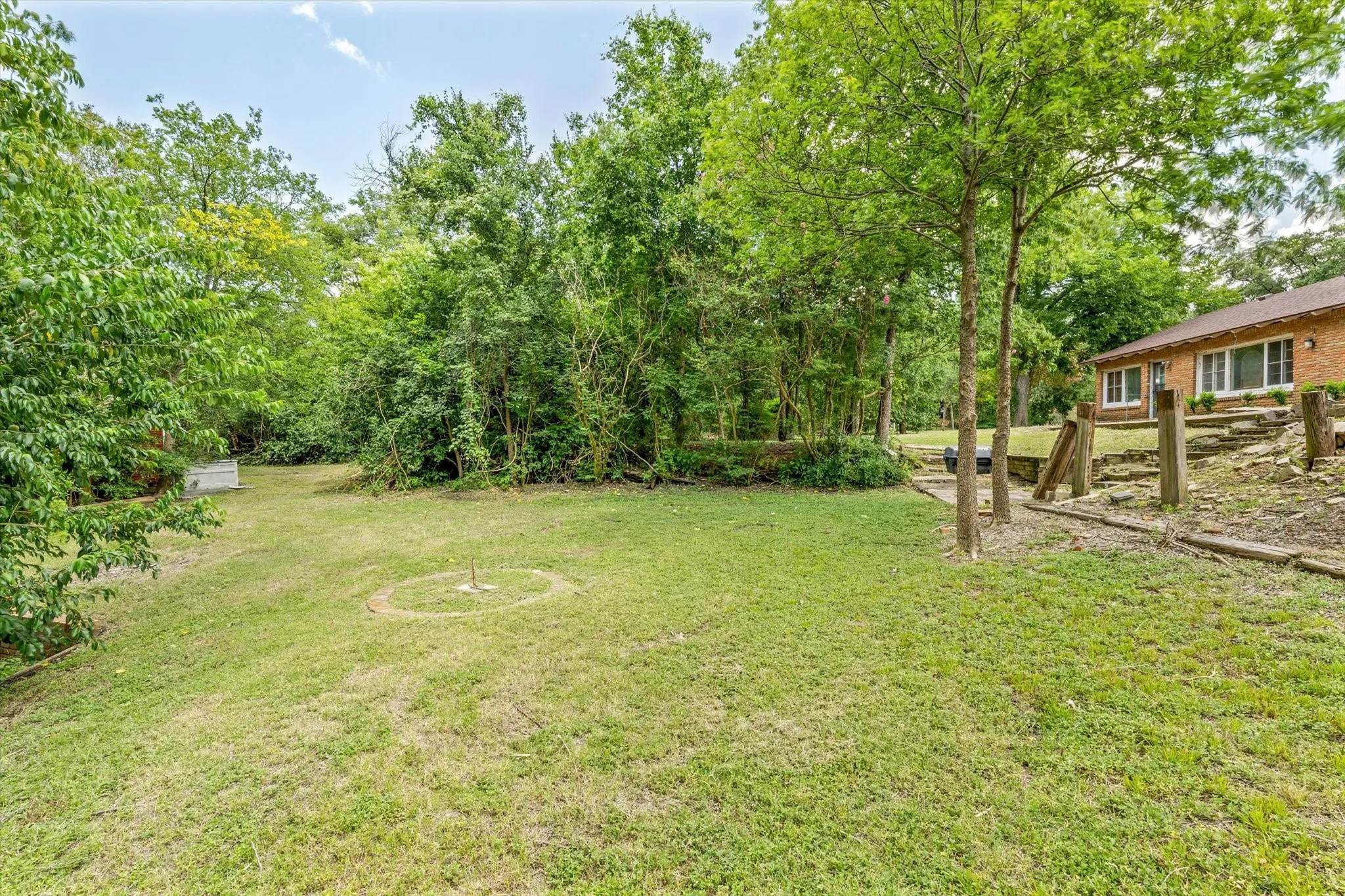 Expansive lawn area with mature trees, a brick exterior residence with multiple windows, and a tiered landscaped hillside