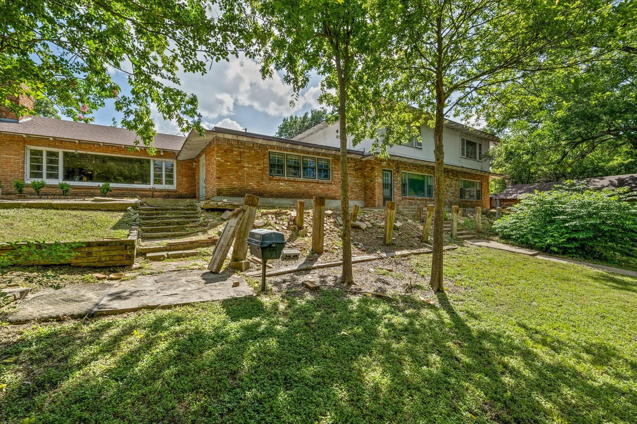 Expansive backyard oasis featuring mature shade trees, manicured lawn, wooden pergola structure, and stone patio with stepped entry