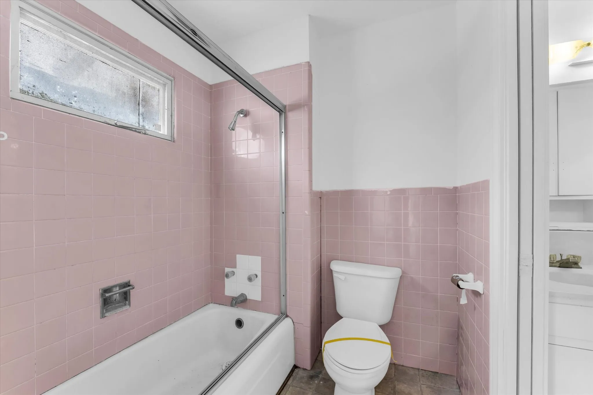 Bathroom featuring a white bathtub, pink tiled walls, a showerhead, and a white toilet