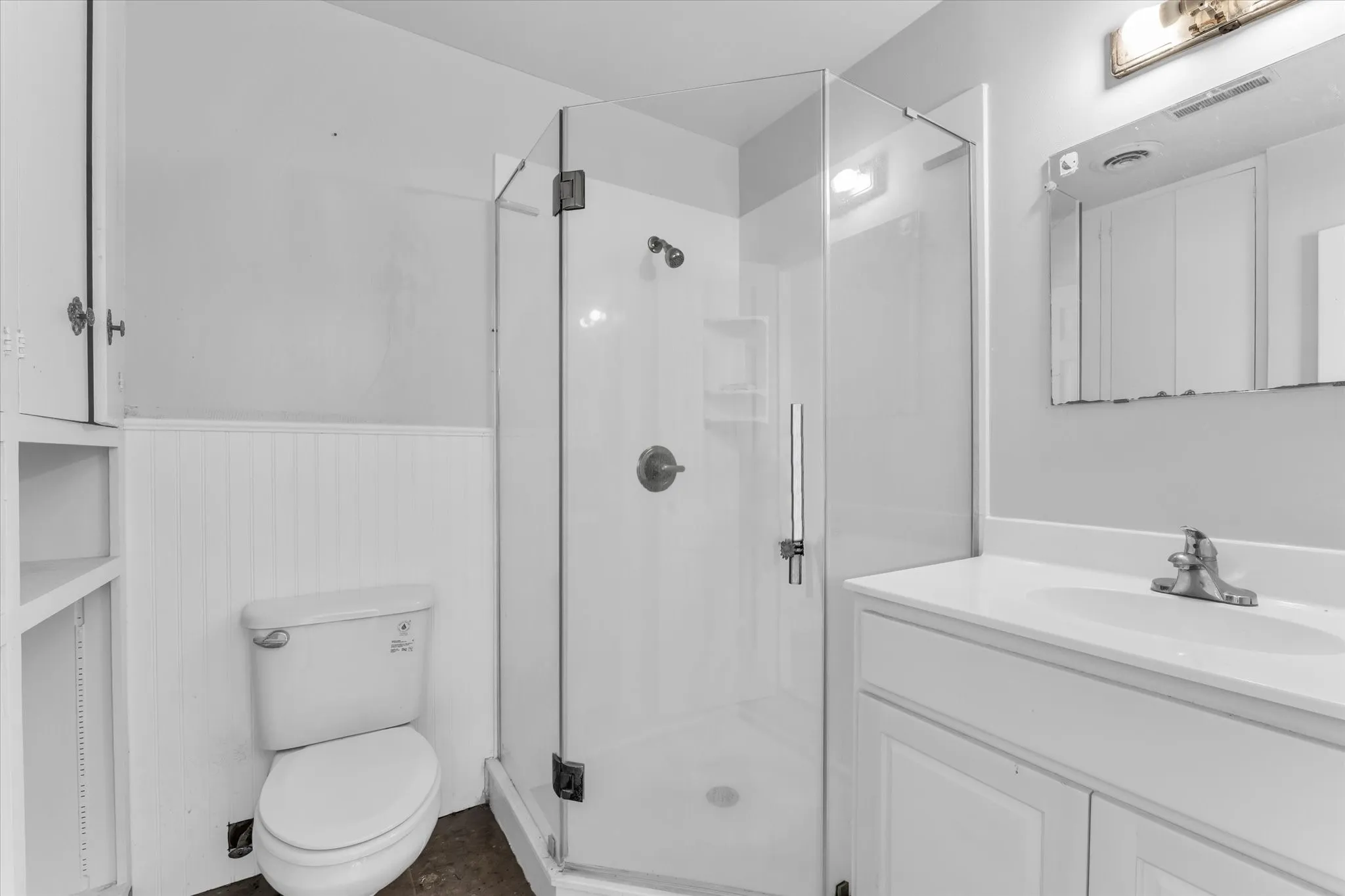 Upstair at the end of the hallway bedroom, bathroom suite, white vanity with integrated sink, glass-enclosed shower, built-in shelving, white beadboard wainscoting, and wall-mounted light fixture