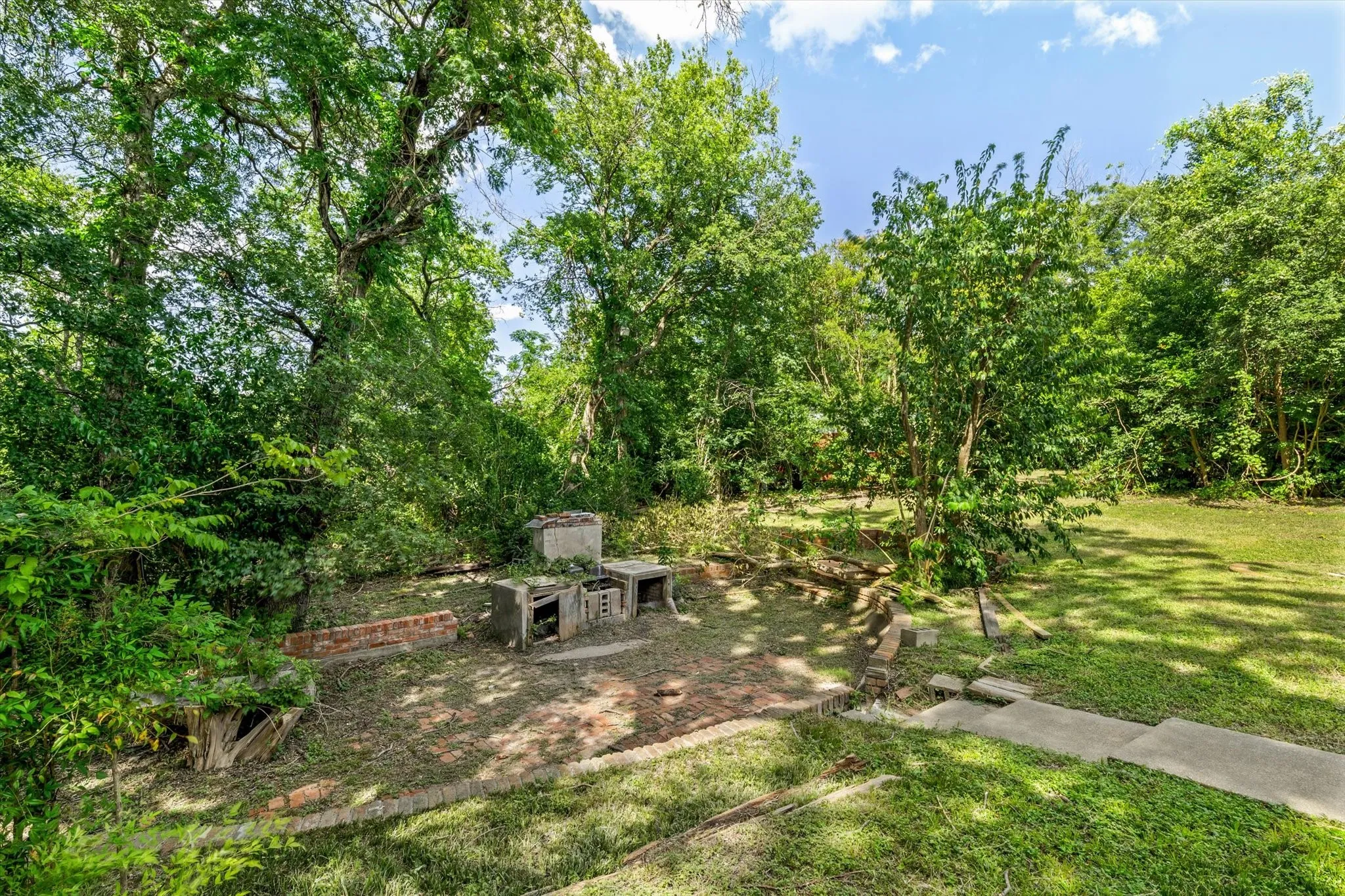 Expansive backyard featuring mature trees, a manicured lawn, and a brick-paved patio area