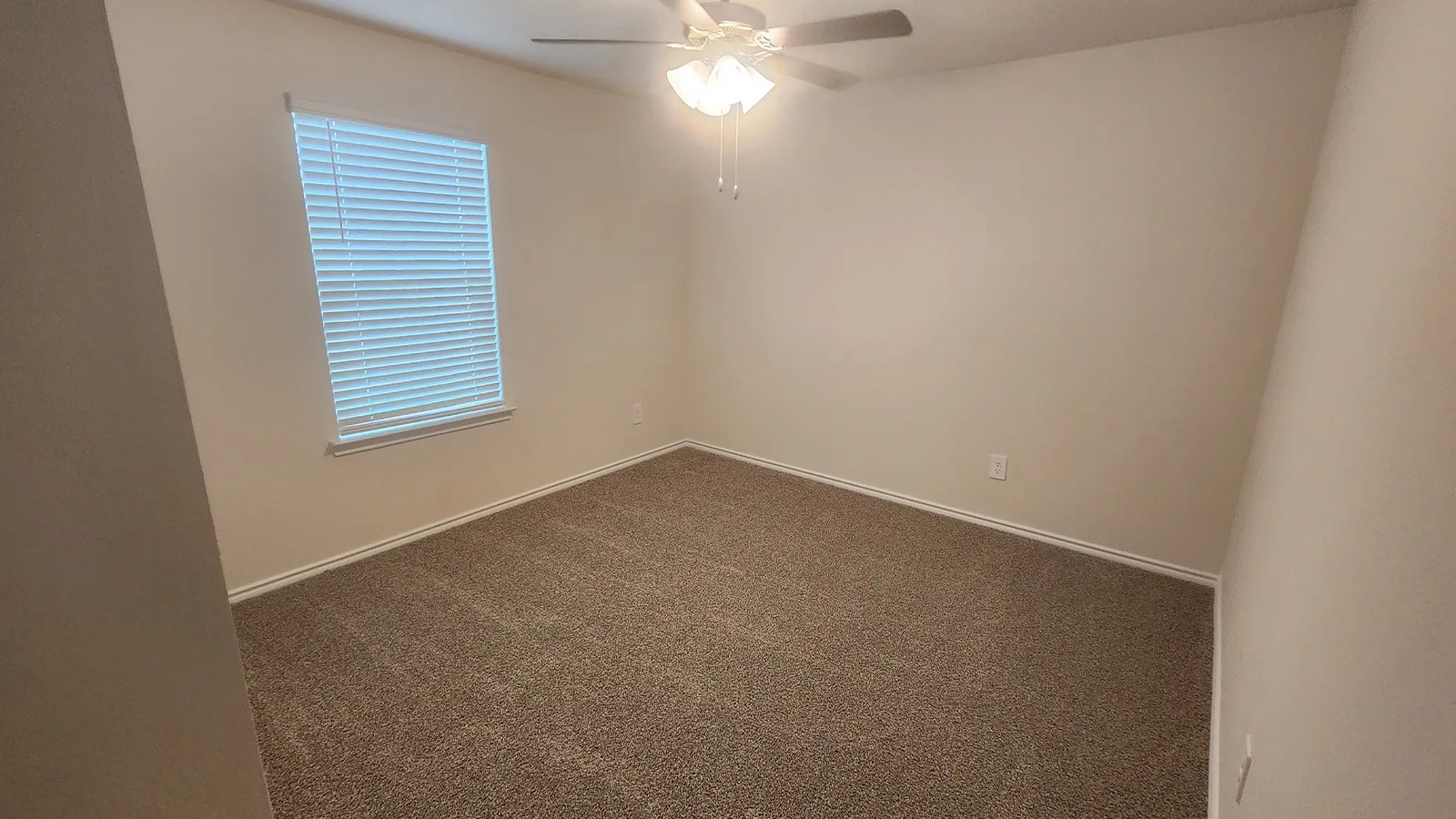 Carpeted room featuring a ceiling fan with integrated lighting and a window with blinds