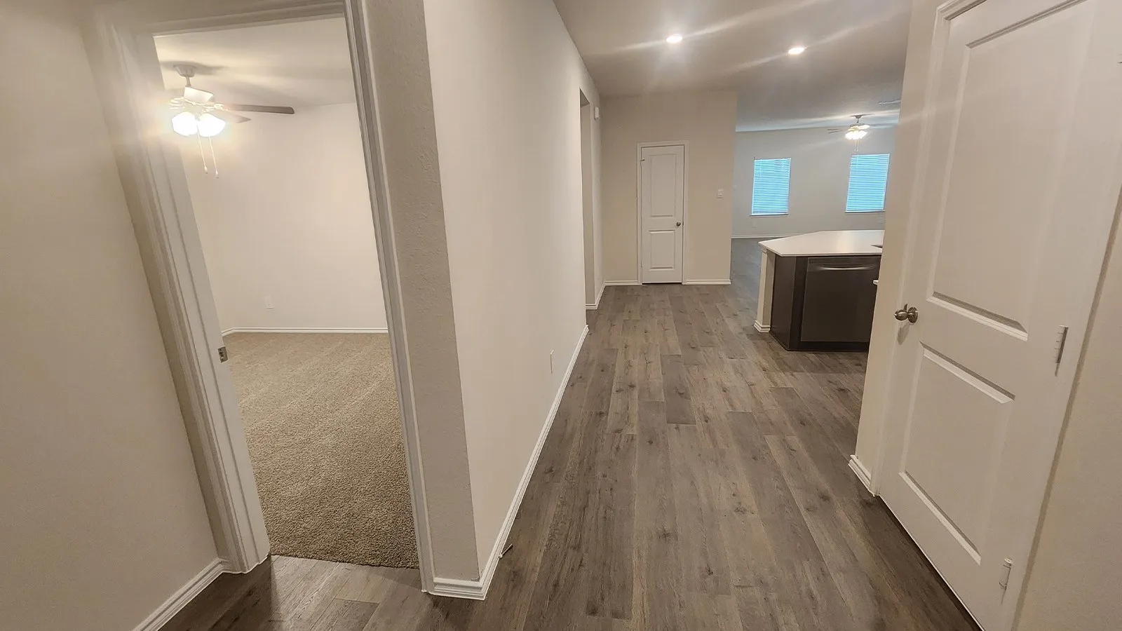 Wood-finish flooring throughout the main hallway, leading to a room with neutral-toned carpeting and a ceiling fan