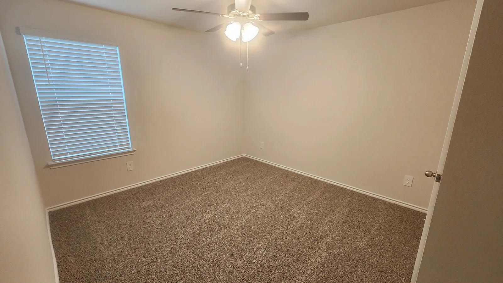 Neutral-toned carpeting, ceiling fan with light fixture, window with blinds, and white trim