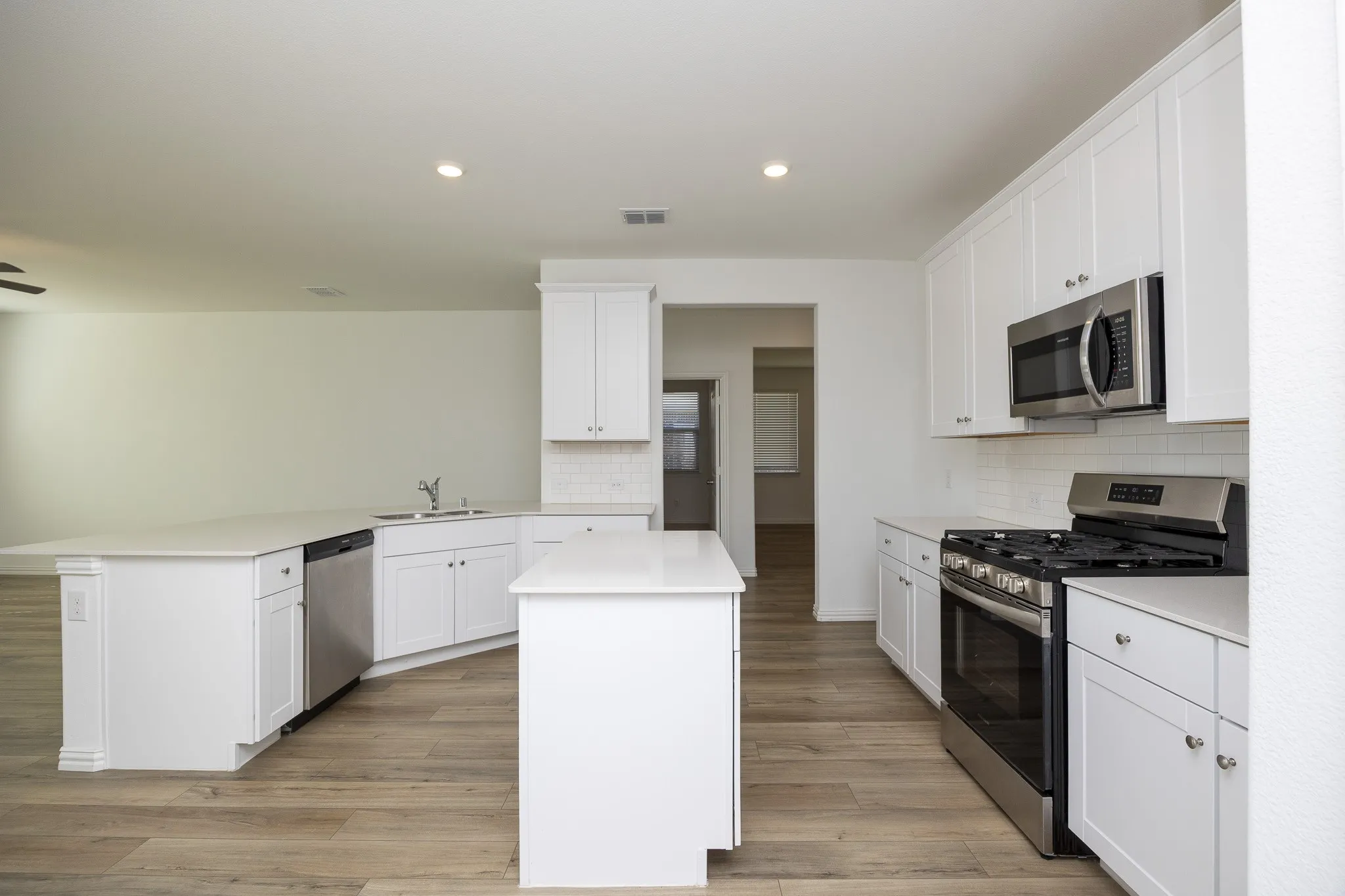 Kitchen featuring white cabinetry, light countertops, stainless steel appliances, and wood-finish flooring