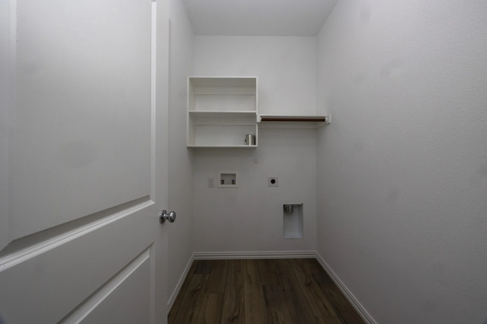 Utility space with wood-finish flooring, built-in shelving, and a hanging rod