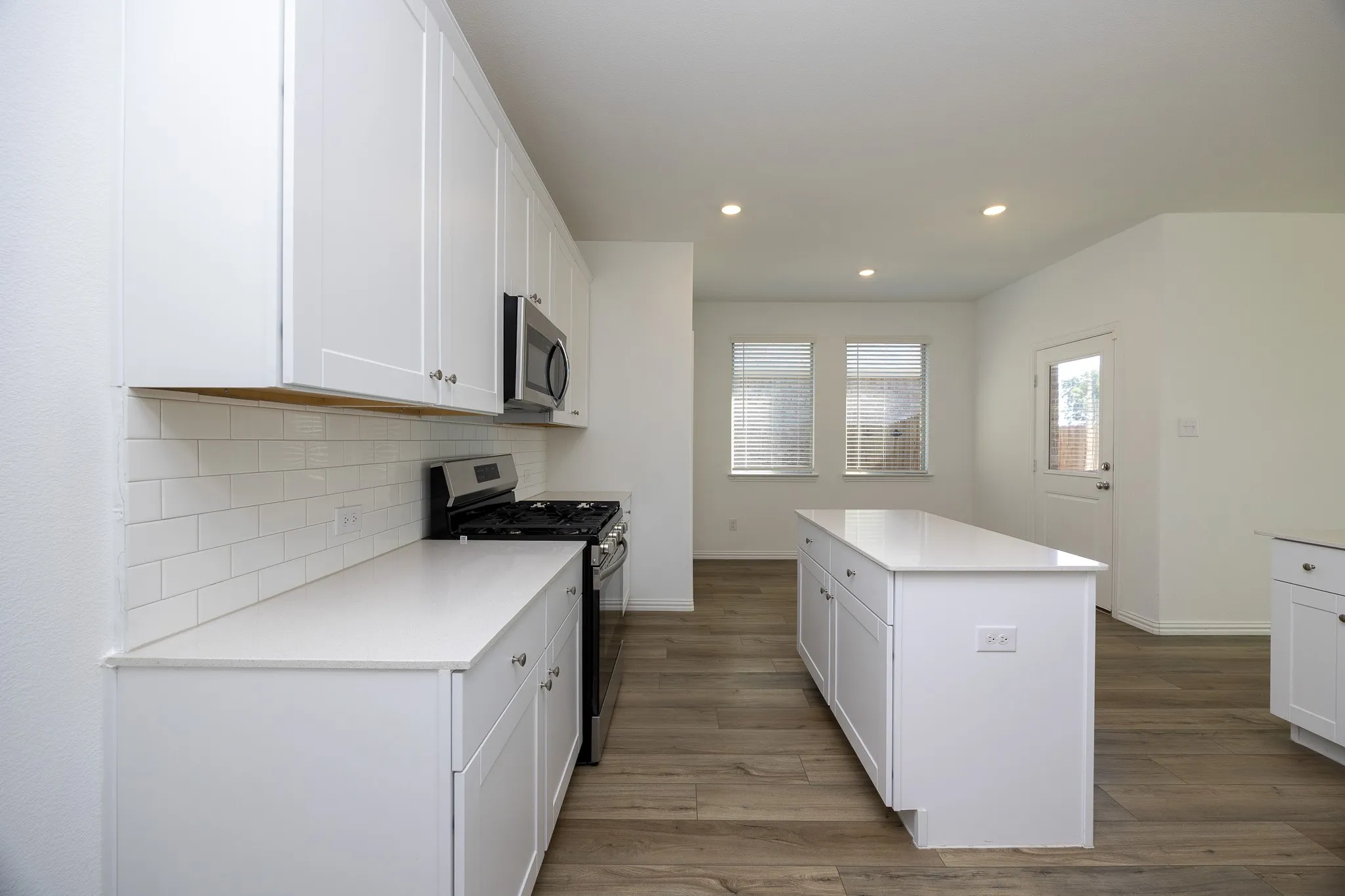 White cabinetry, subway tile backsplash, white countertops, stainless steel appliances, and wood-finish flooring
