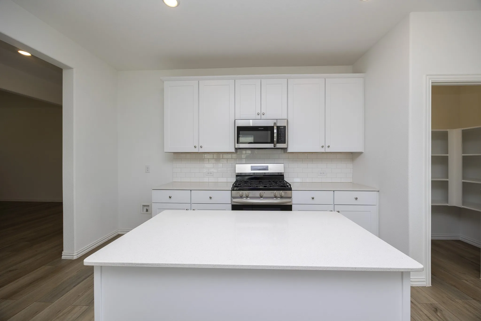 Kitchen featuring white cabinetry, a central island with a light-toned countertop, stainless steel appliances, and a subway tile backsplash
