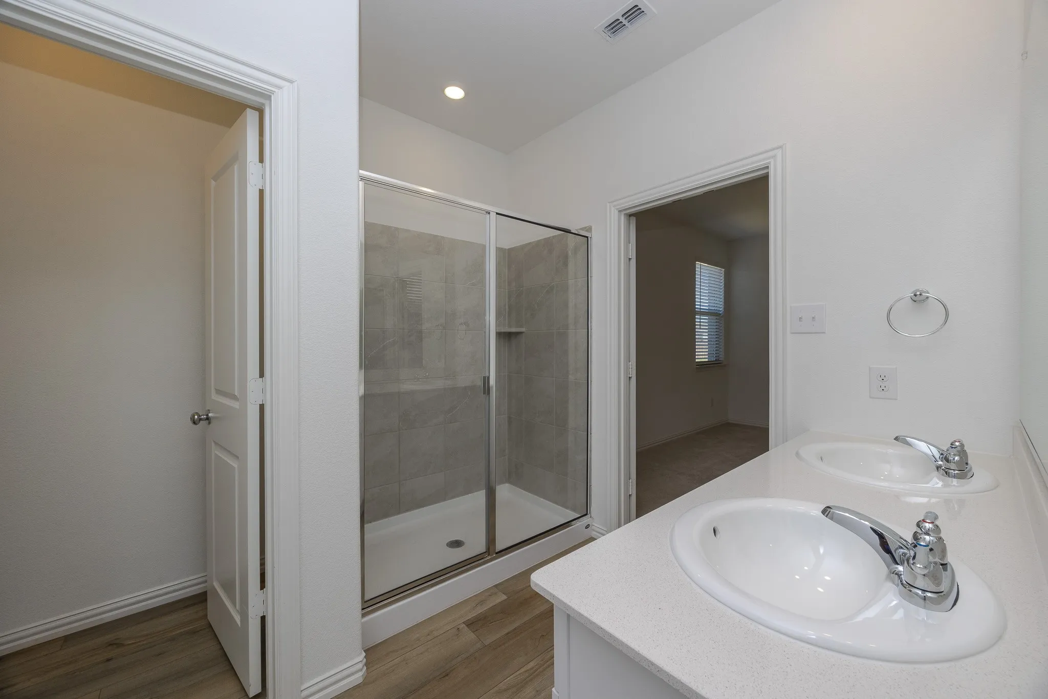 Dual white oval sinks with chrome faucets, a light-toned countertop, and a glass-enclosed shower with tiled walls