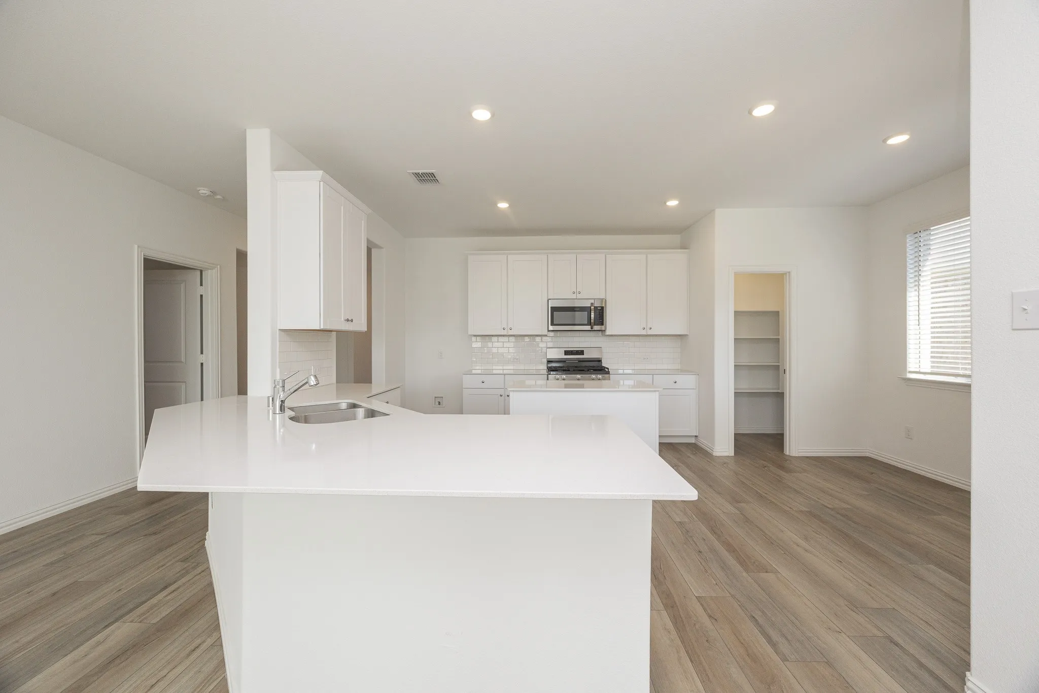 White shaker cabinetry, recessed lighting, wood-finish flooring, stainless steel appliances, and a walk-in pantry