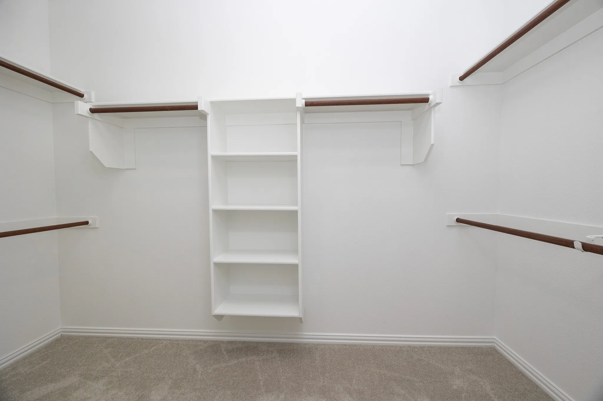Built-in shelving unit, multiple clothing rods, and light-toned carpeting