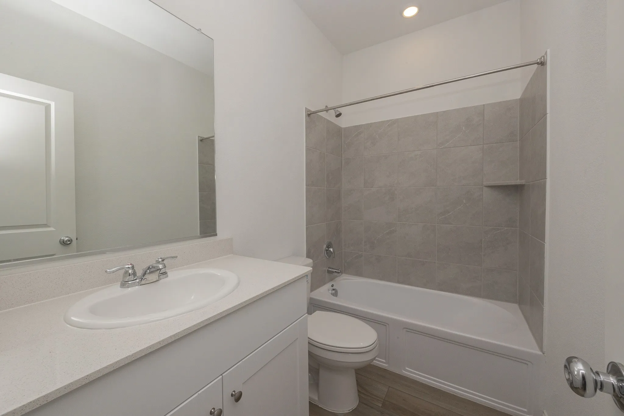 Bathroom featuring a built-in vanity with an integrated sink, polished chrome faucet, a large wall-mounted mirror, a tub/shower combination with tile surround, and wood-finish flooring