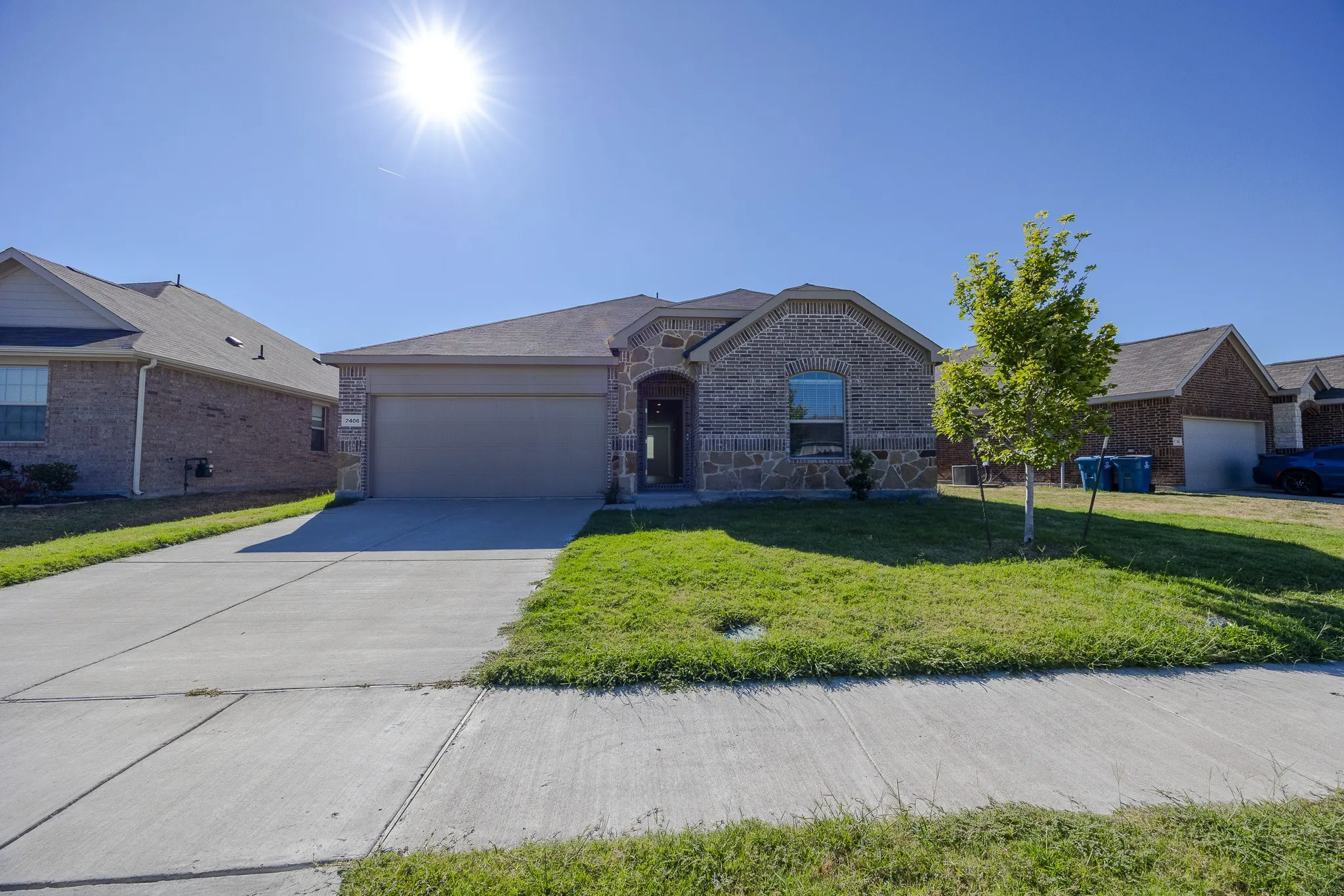 Brick and stone facade, attached garage, concrete driveway, and front lawn