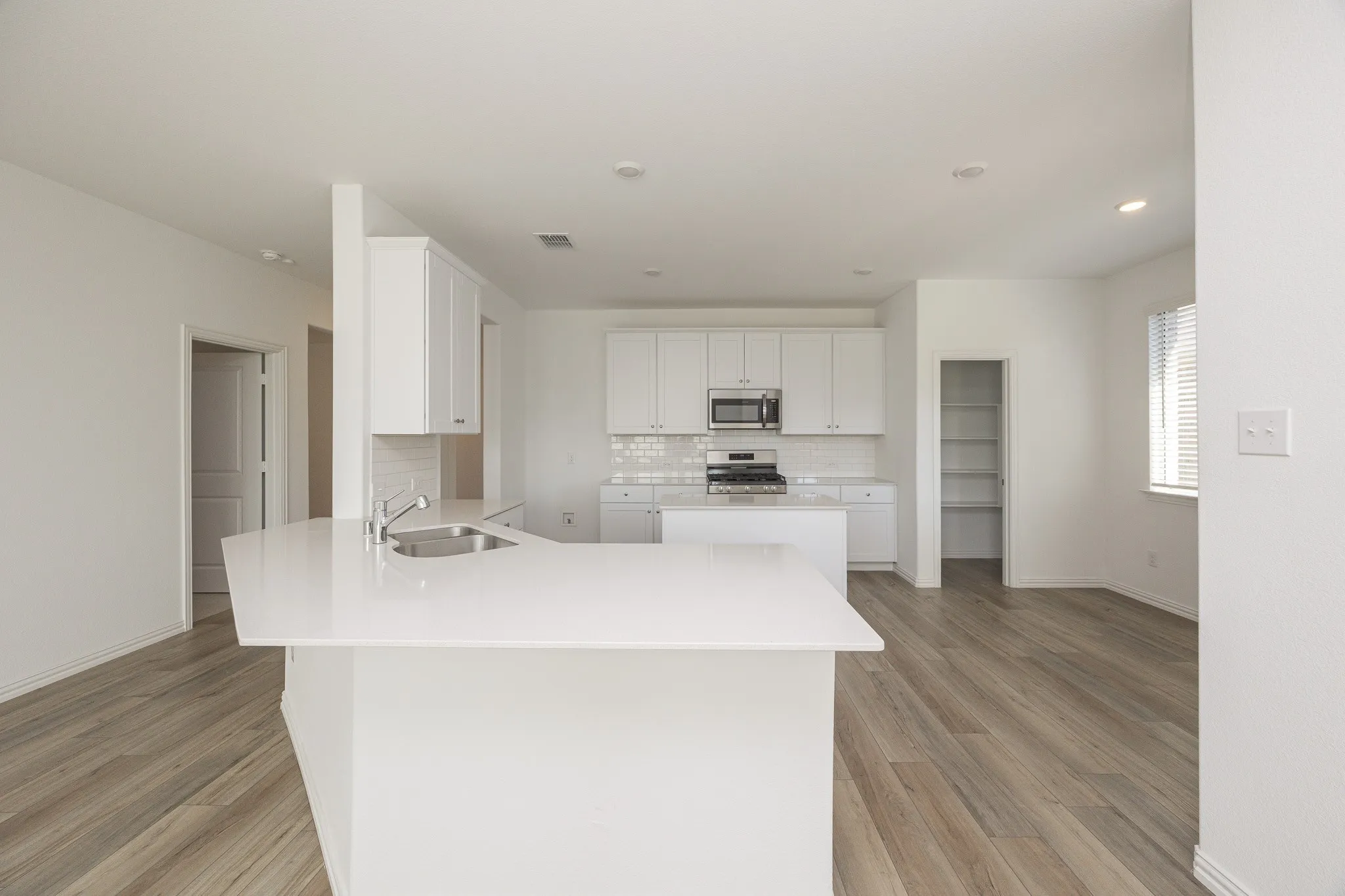 Open-concept living area featuring a kitchen with white cabinetry, stainless steel appliances, a white tile backsplash, and a kitchen island with a sink