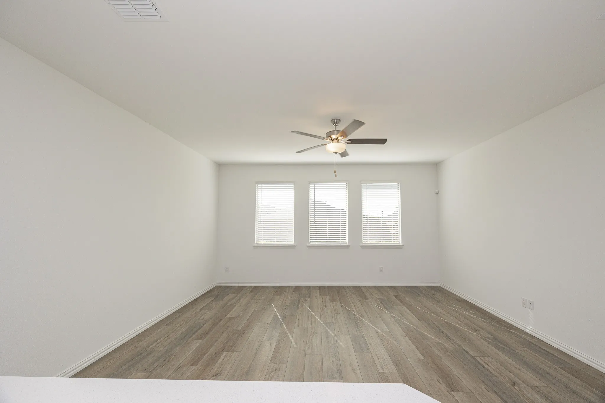 Wood-finish flooring, three windows with blinds, and a ceiling fan with integrated lighting