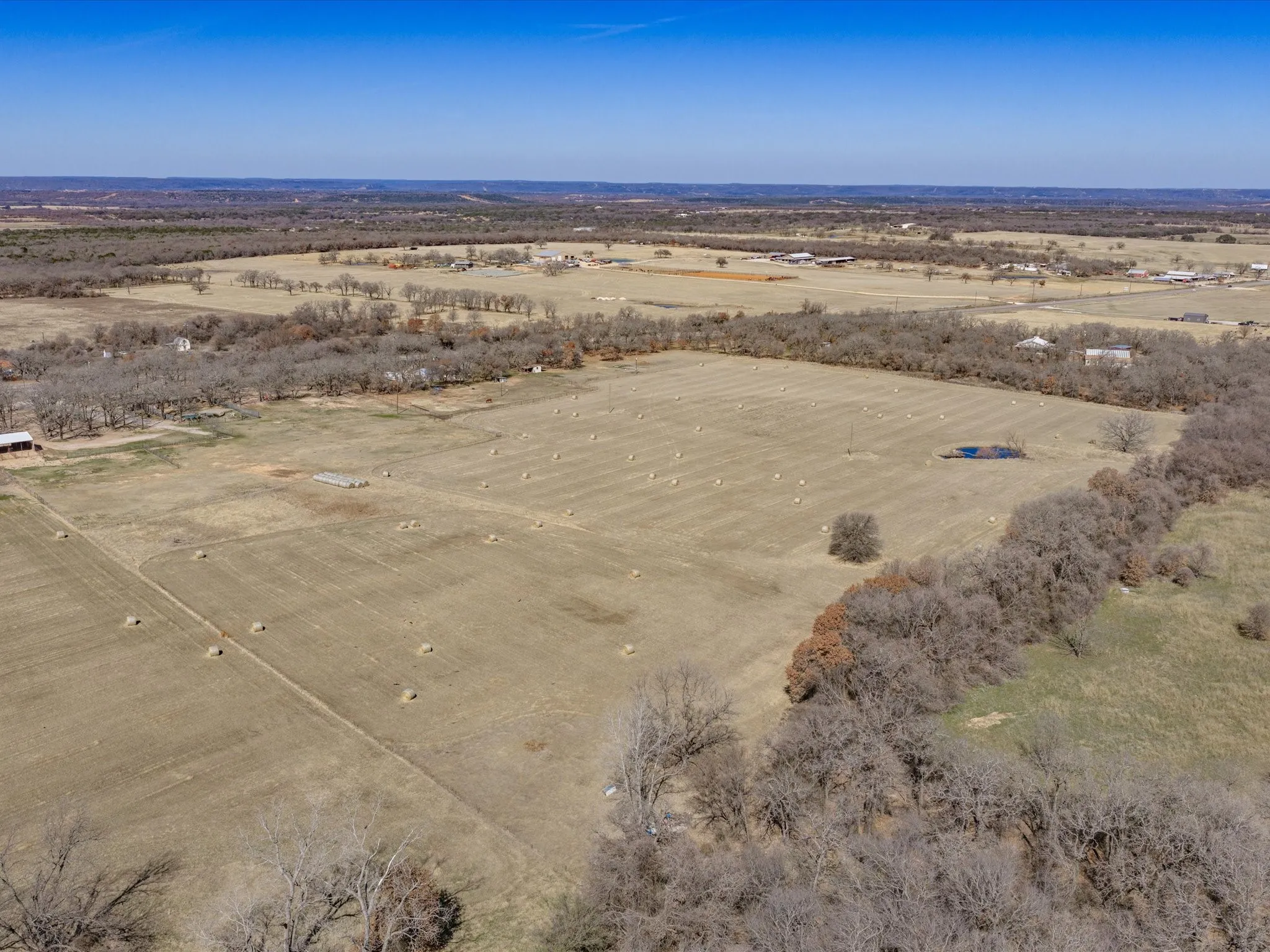 Expansive undeveloped acreage featuring a natural tree line, hay bales, and a small pond