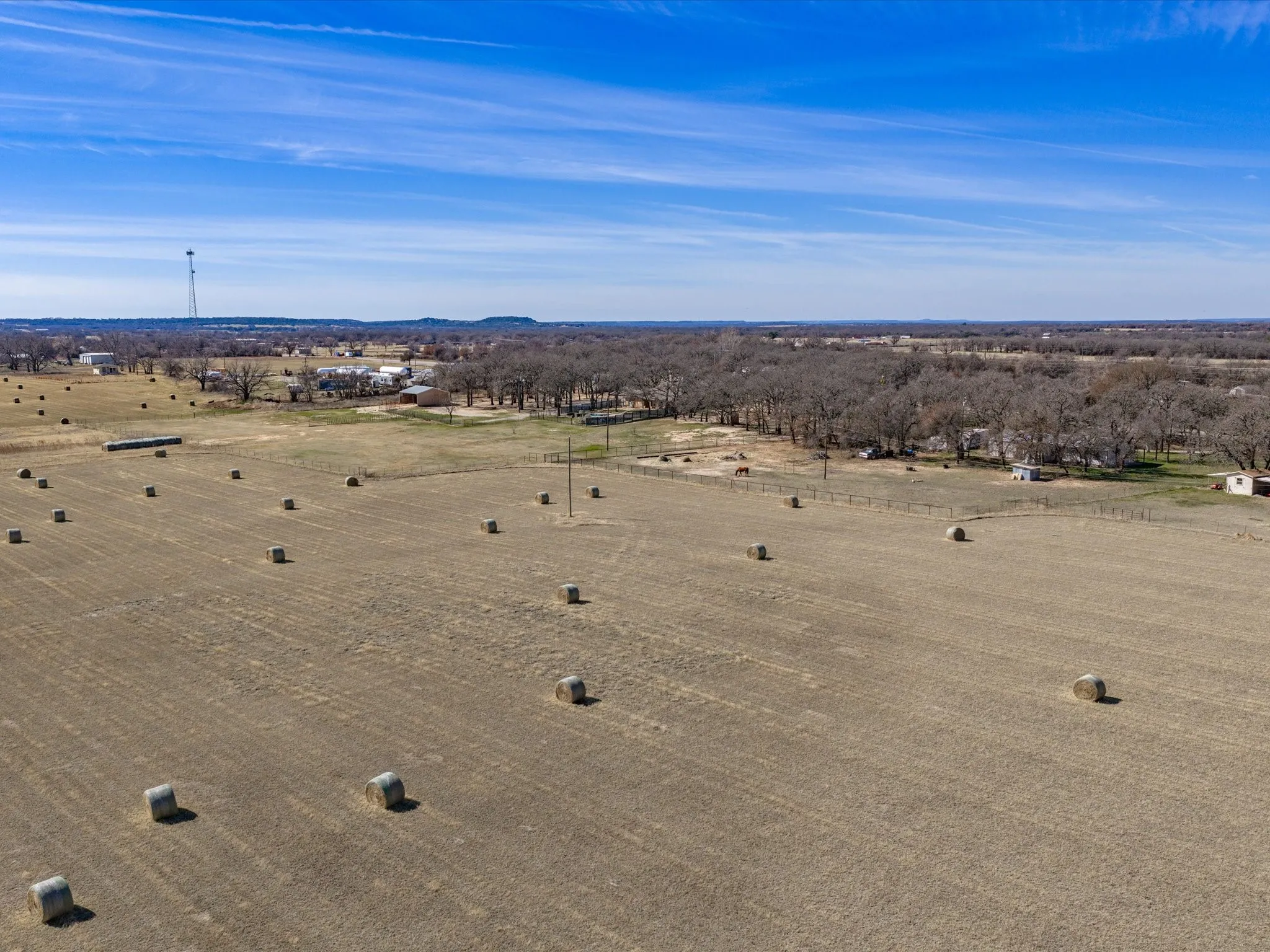 Expansive land parcel featuring open fields, scattered hay bales, and distant tree lines