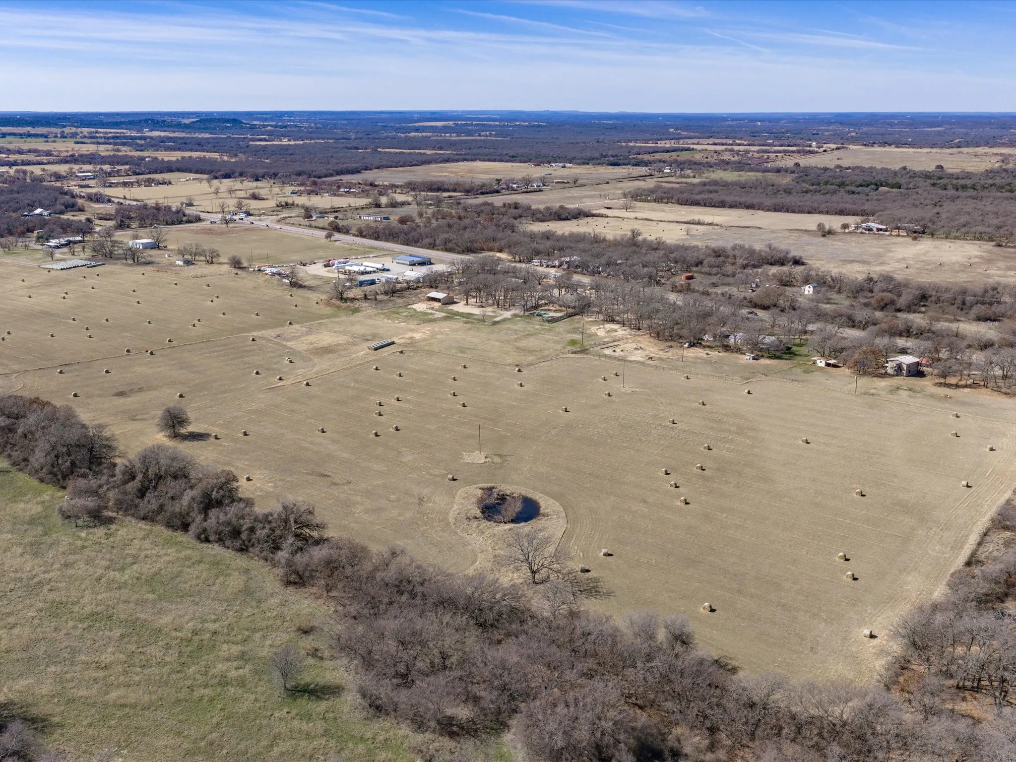 Expansive rural landscape featuring open fields, scattered trees, and a natural pond