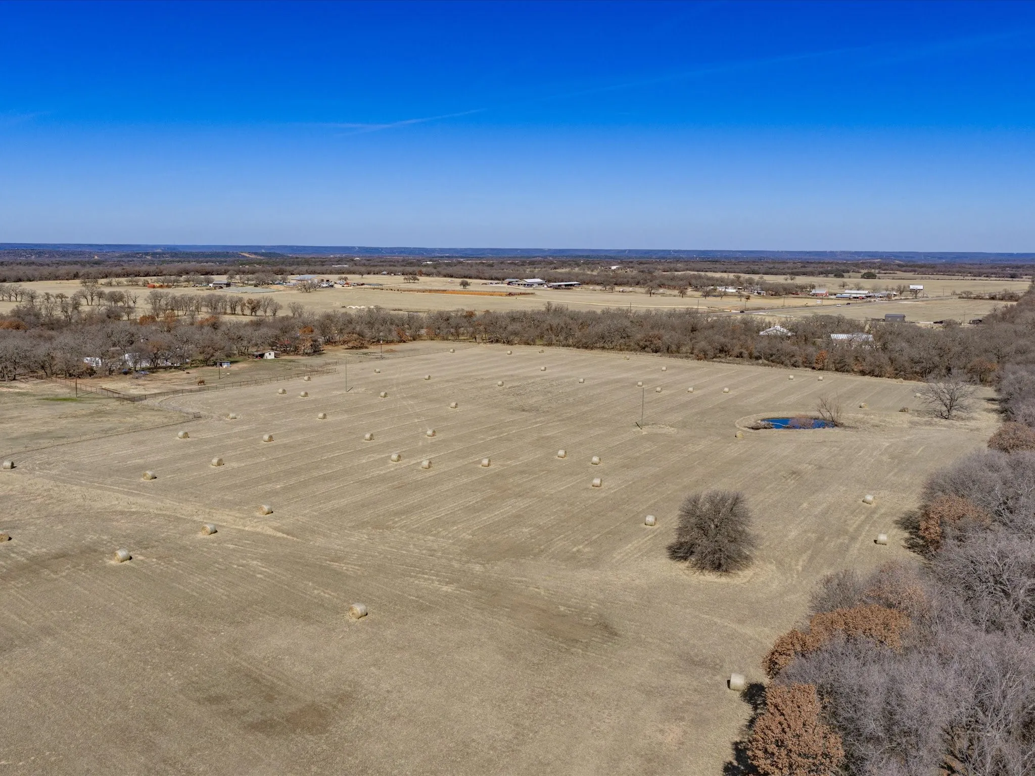 Expansive agricultural land featuring a field with hay bales and a natural pond