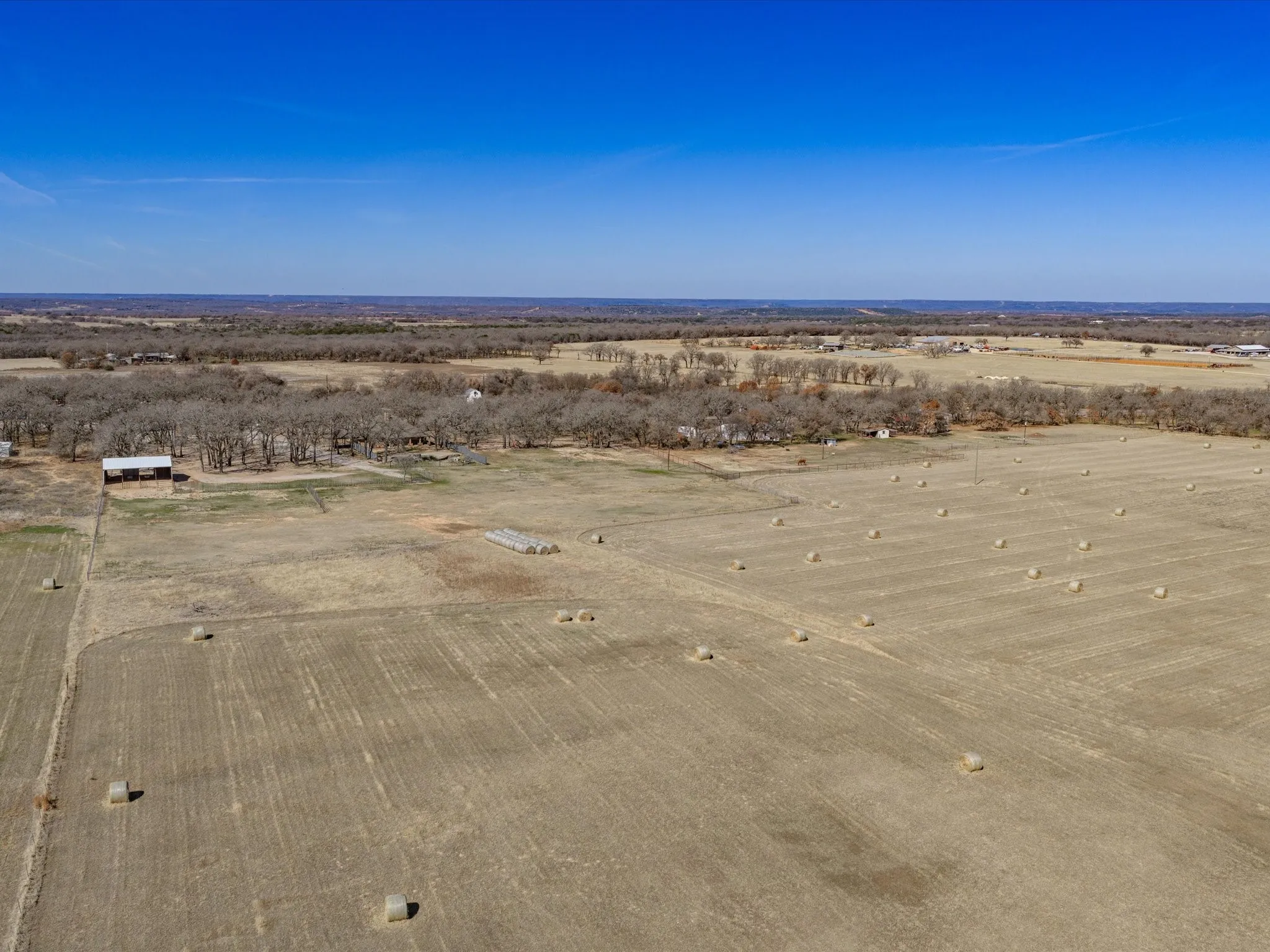 Expansive open land with cultivated fields, scattered hay bales, and distant tree lines
