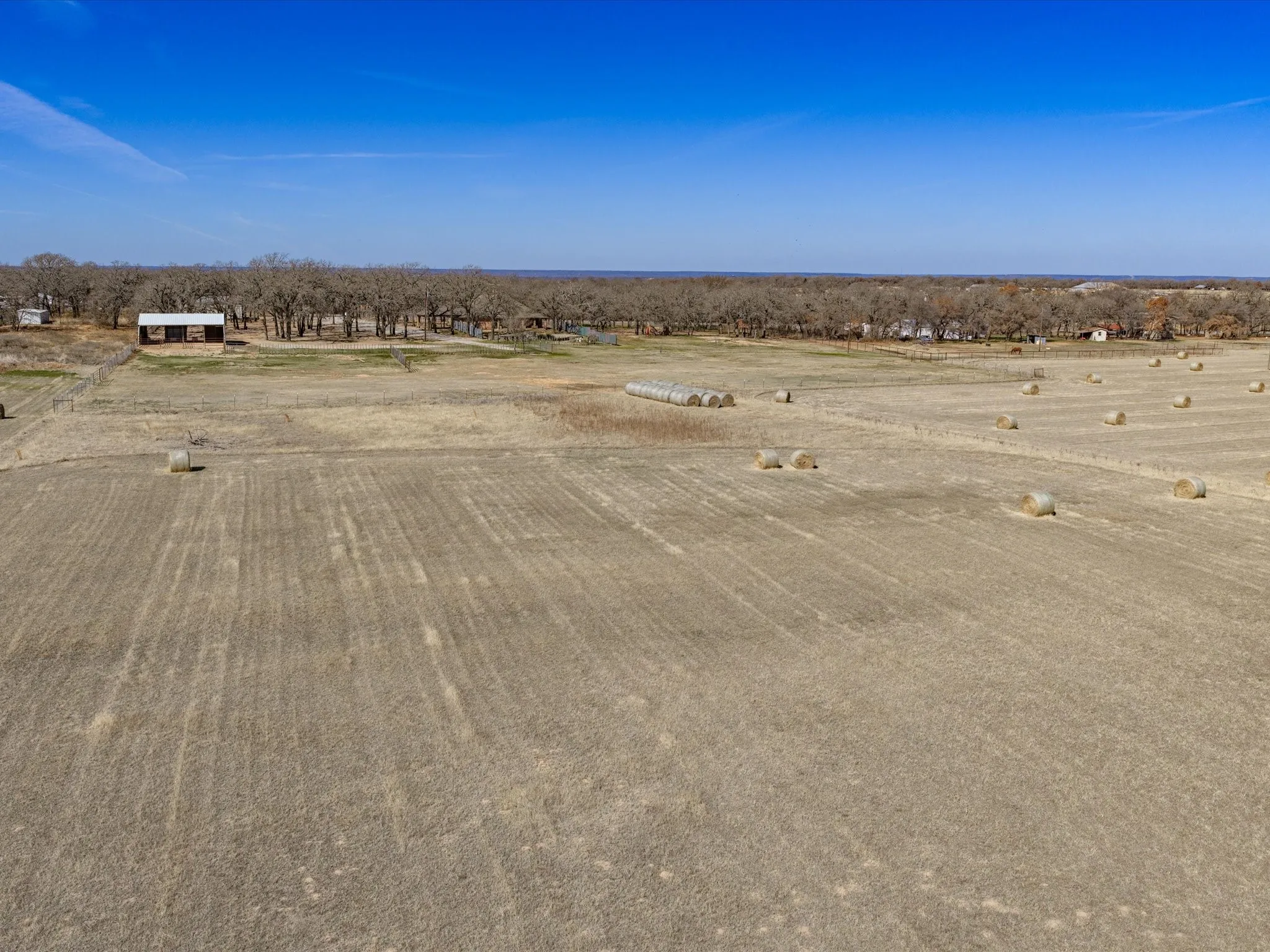 Expansive land with visible hay bales, distant structures, and tree lines
