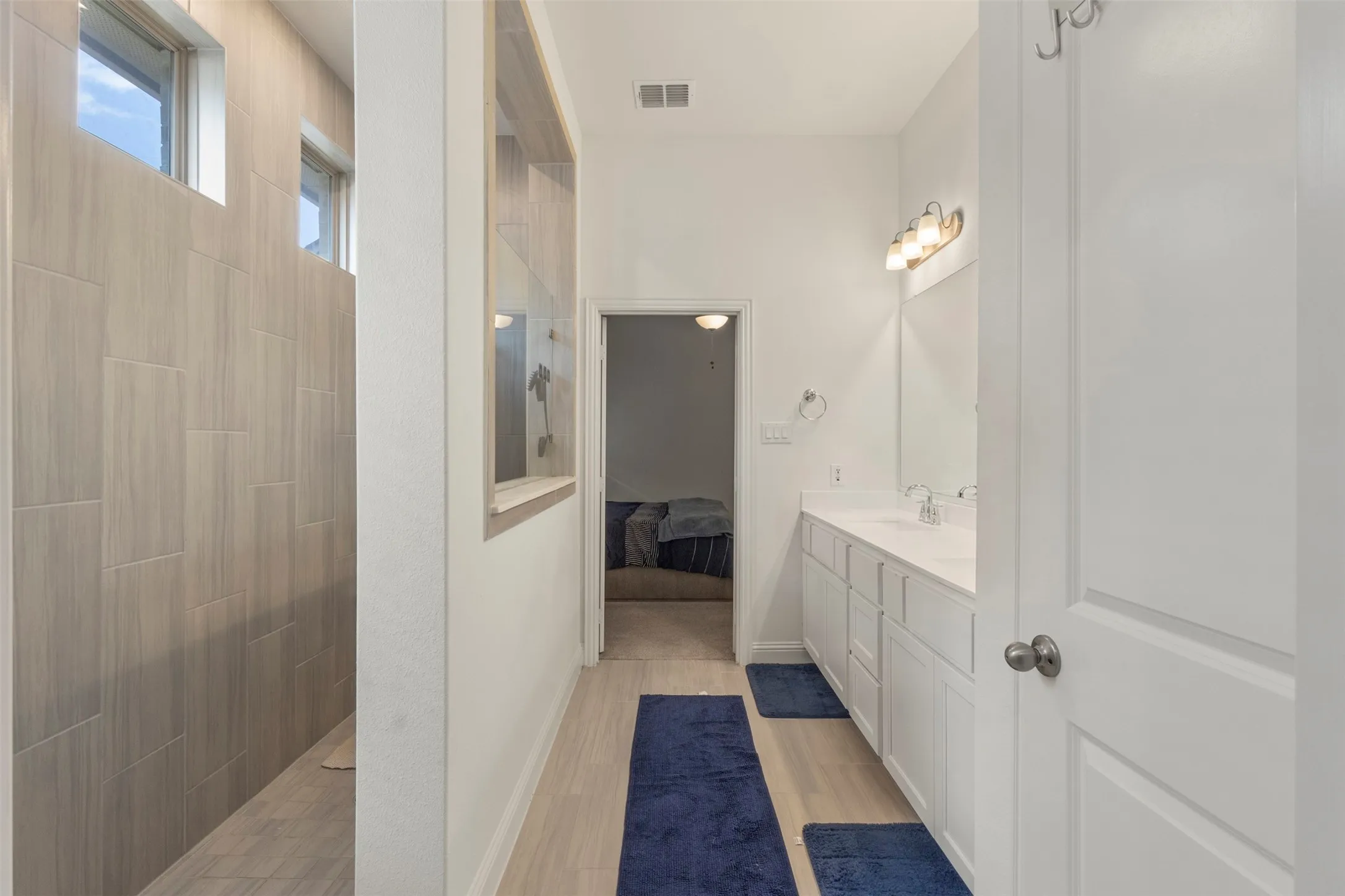 Bathroom featuring a dual vanity, wood-finish flooring, a tiled shower, and transom windows