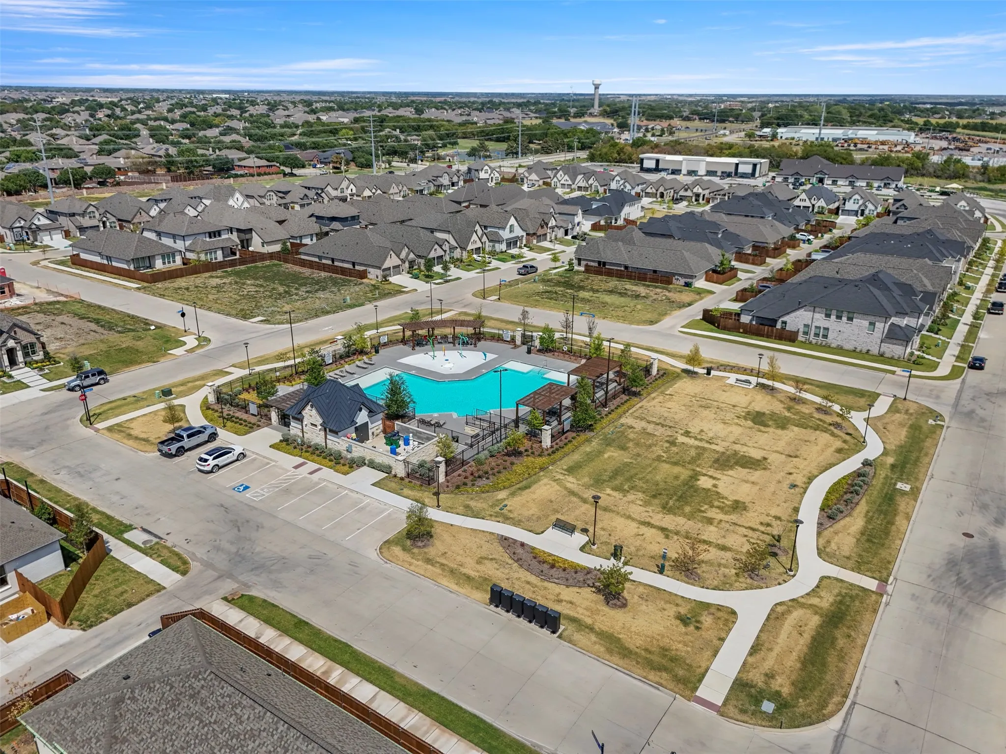 Community pool with adjacent recreational lawn area, bordered by sidewalks and residential streets