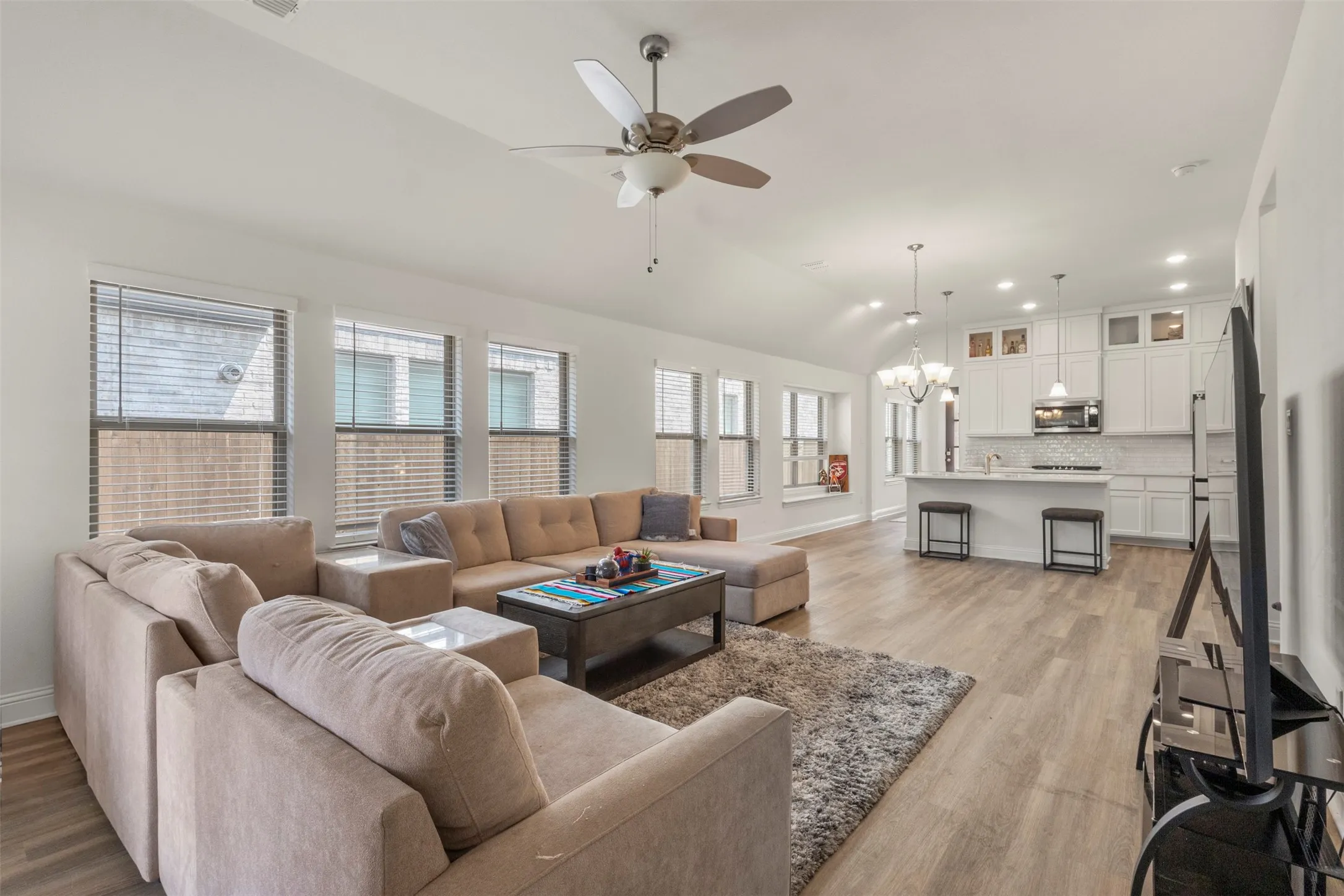 Vaulted ceilings, wood-finish flooring, white cabinetry, integrated stainless steel appliances, and a kitchen island with pendant lighting