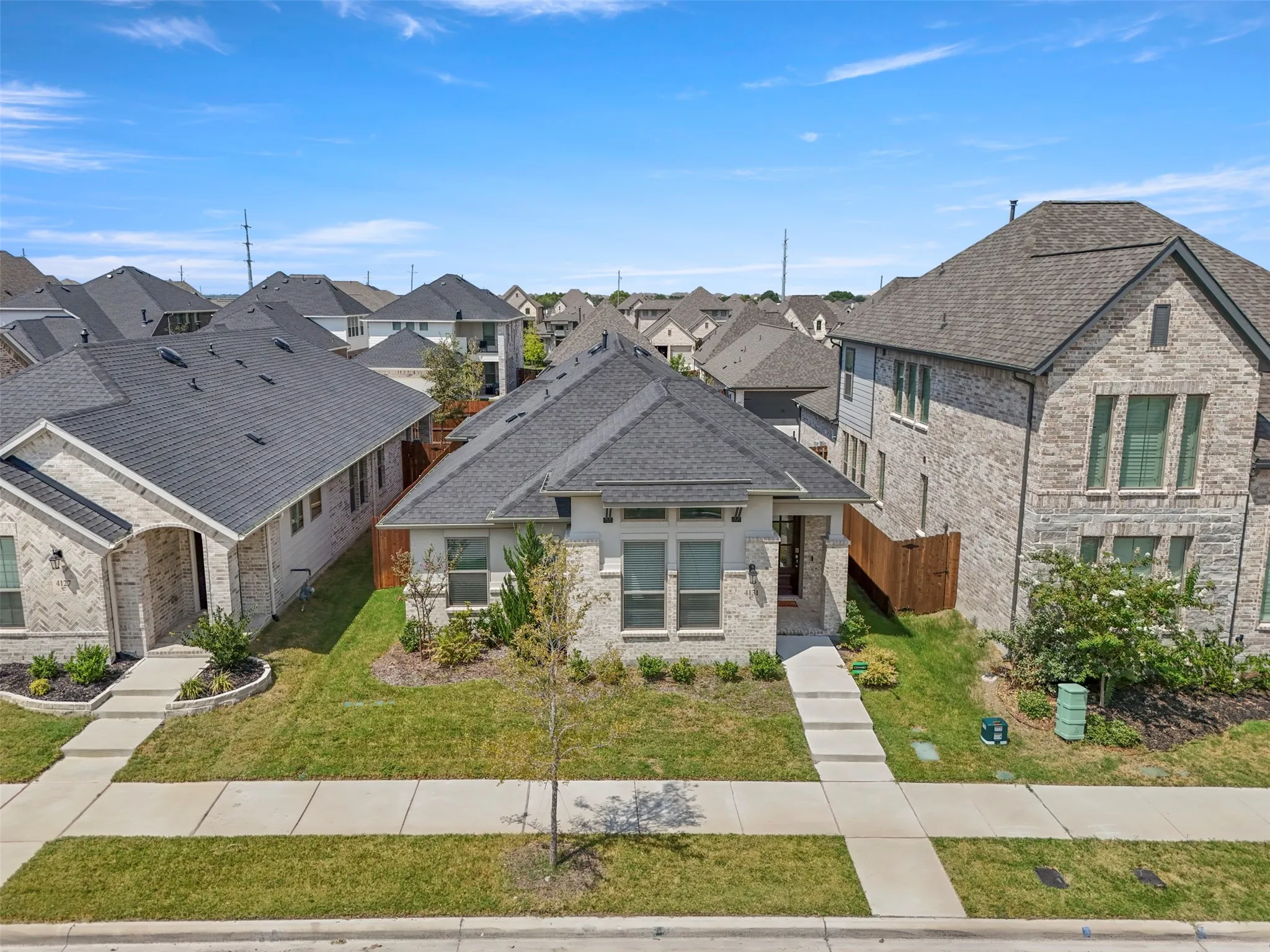 Light-colored brick exterior with stone accents, dark-toned shingle roof, well-maintained front lawn, and concrete walkways