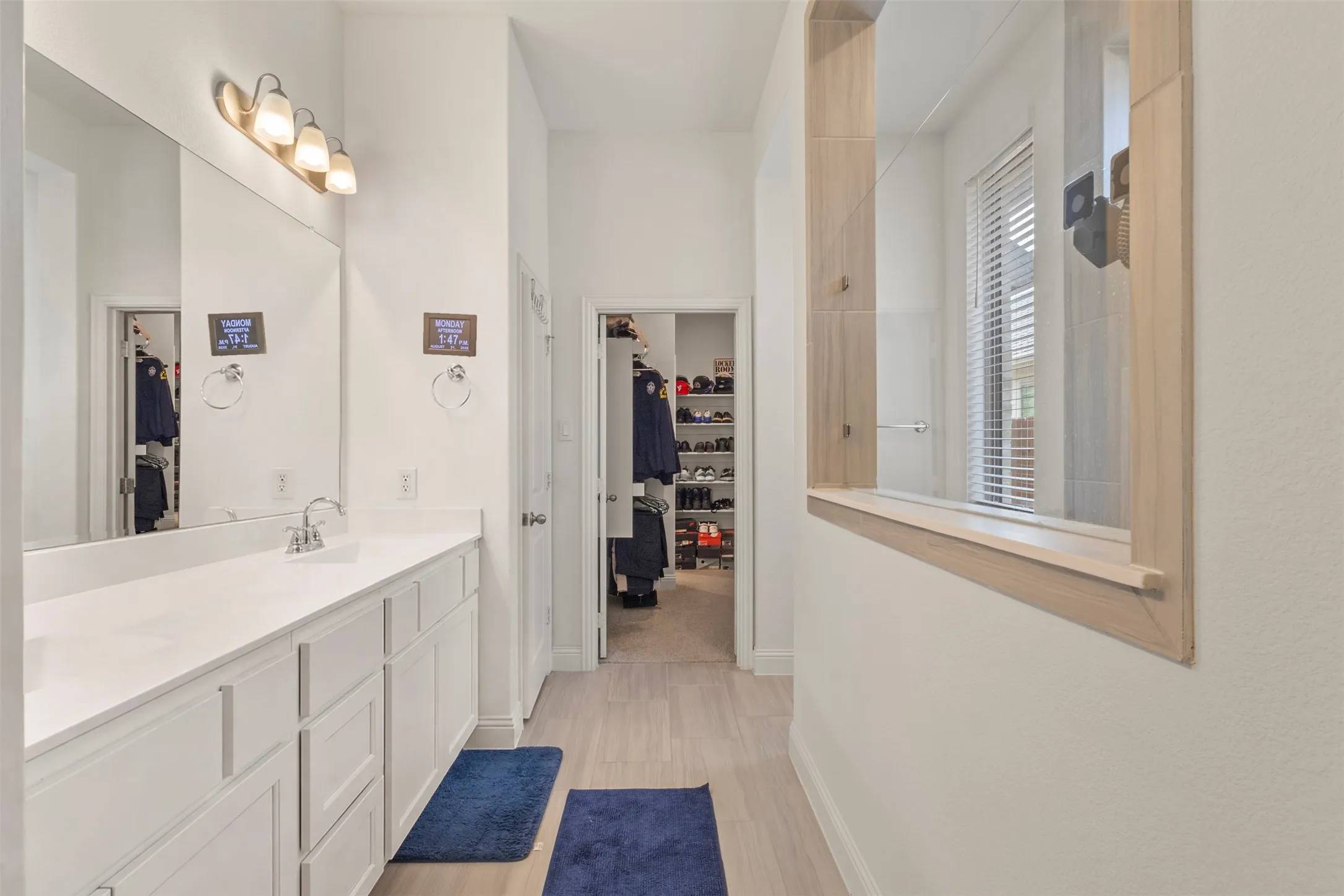 Long white vanity with dual sinks and chrome fixtures, illuminated by a three-light vanity bar
