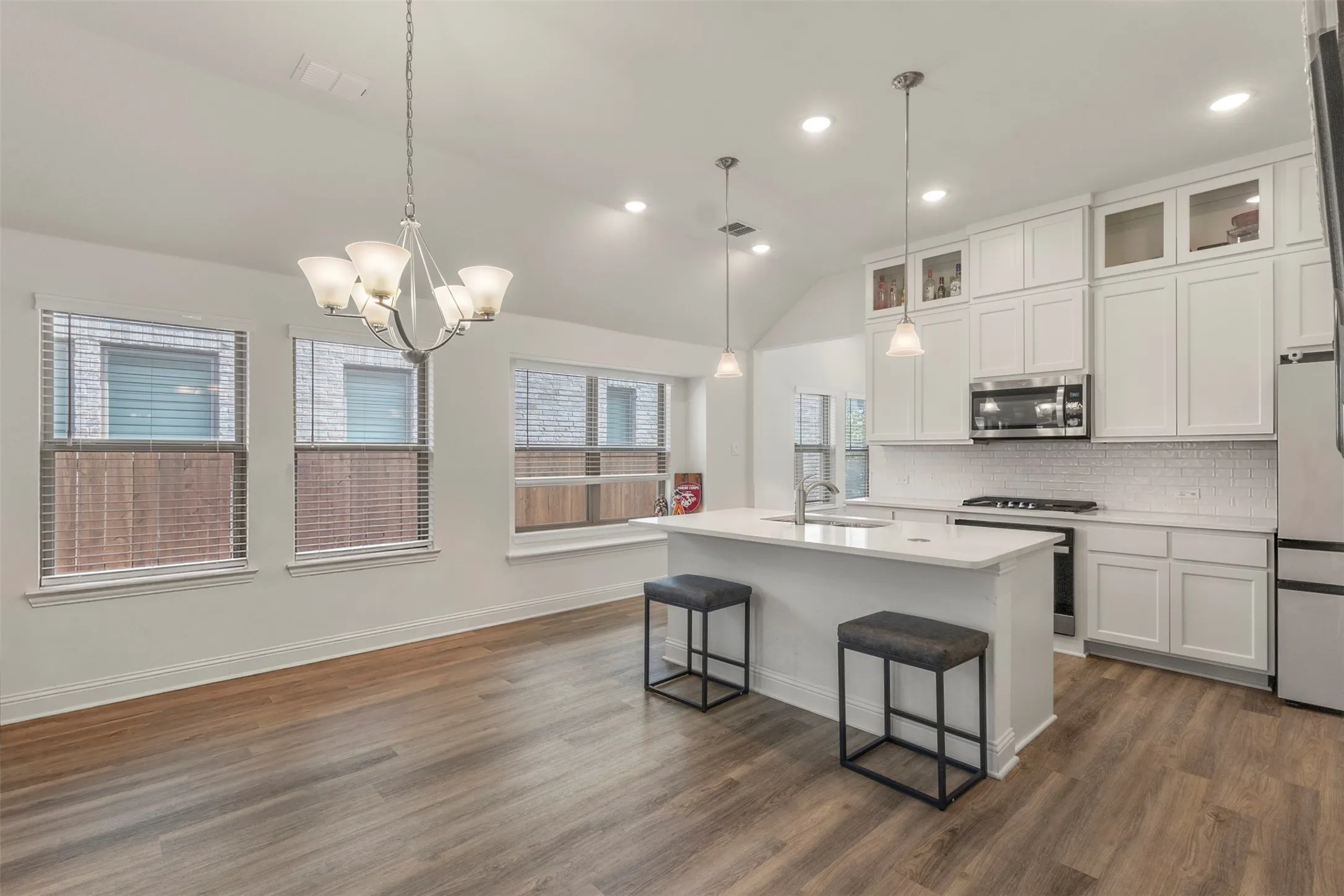 Open-concept kitchen and dining area featuring wood-finish flooring, a kitchen island with an integrated sink, white cabinetry, and stainless steel appliances