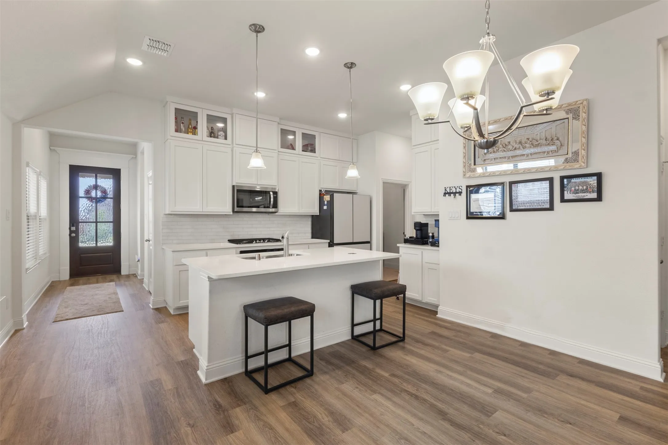Open-concept kitchen with white cabinetry, stainless steel appliances, a center island with seating, and wood-finish flooring throughout