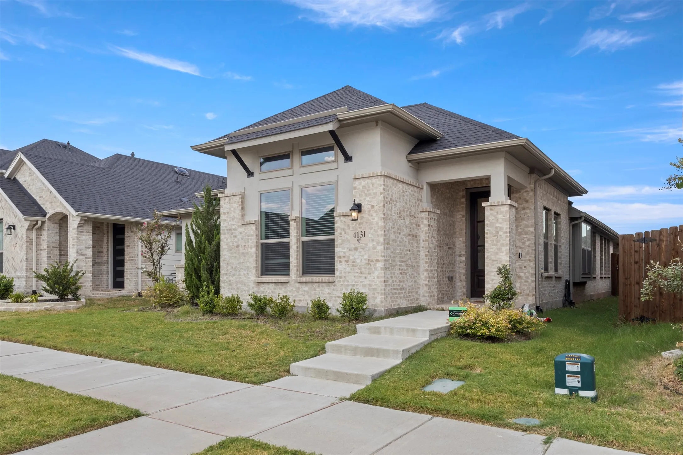 Brick and stucco exterior with a dark-pitched roof, large windows, an integrated porch, and a concrete pathway
