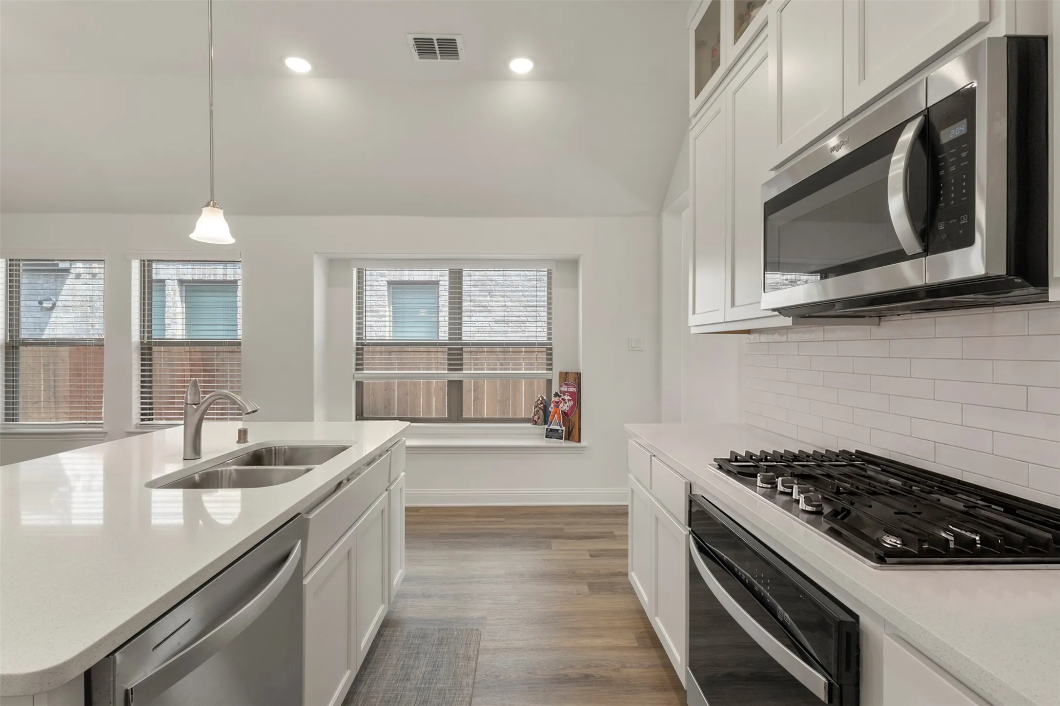 Kitchen featuring a center island with sink, white shaker cabinetry, stainless steel appliances, and wood-finish flooring
