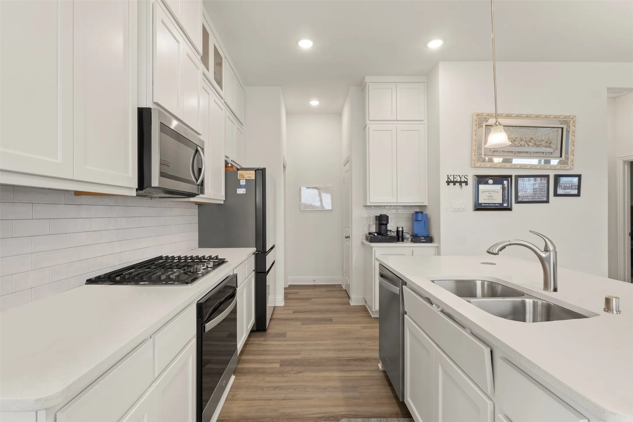 Contemporary kitchen featuring white cabinetry, stainless steel appliances, a gas cooktop, white subway tile backsplash, and wood-finish flooring