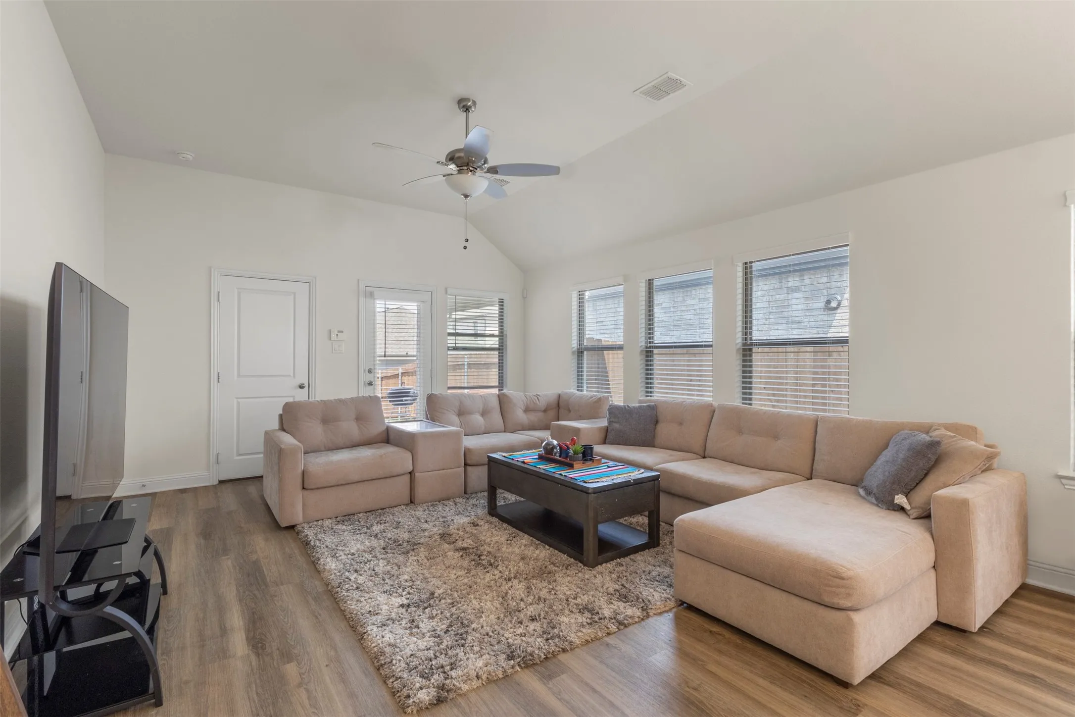 Vaulted ceiling with a ceiling fan, wood-finish flooring, multiple windows with blinds, and a white paneled door