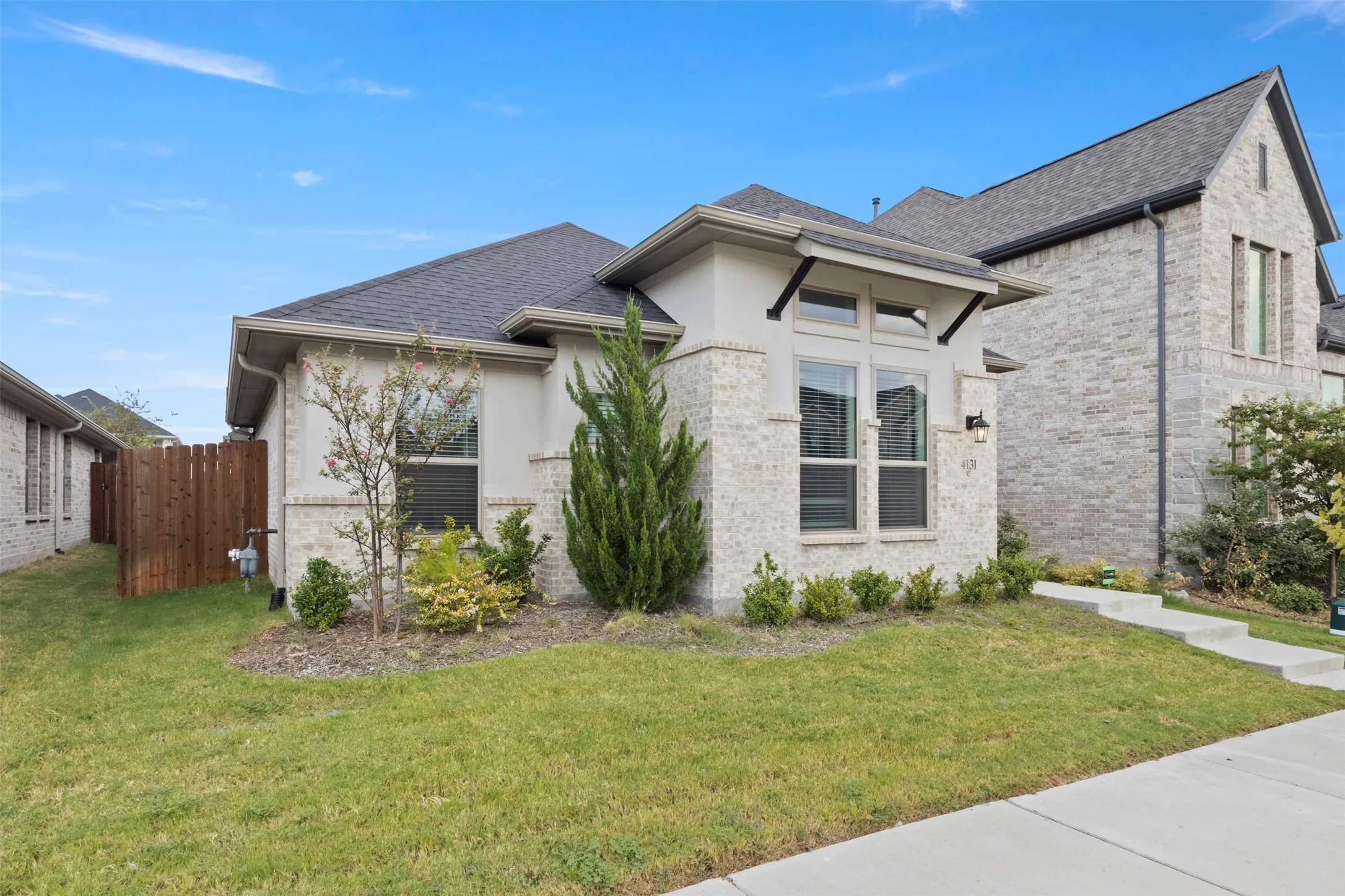 Contemporary exterior with brick and stucco facade, a dark shingle roof, and a wood privacy fence