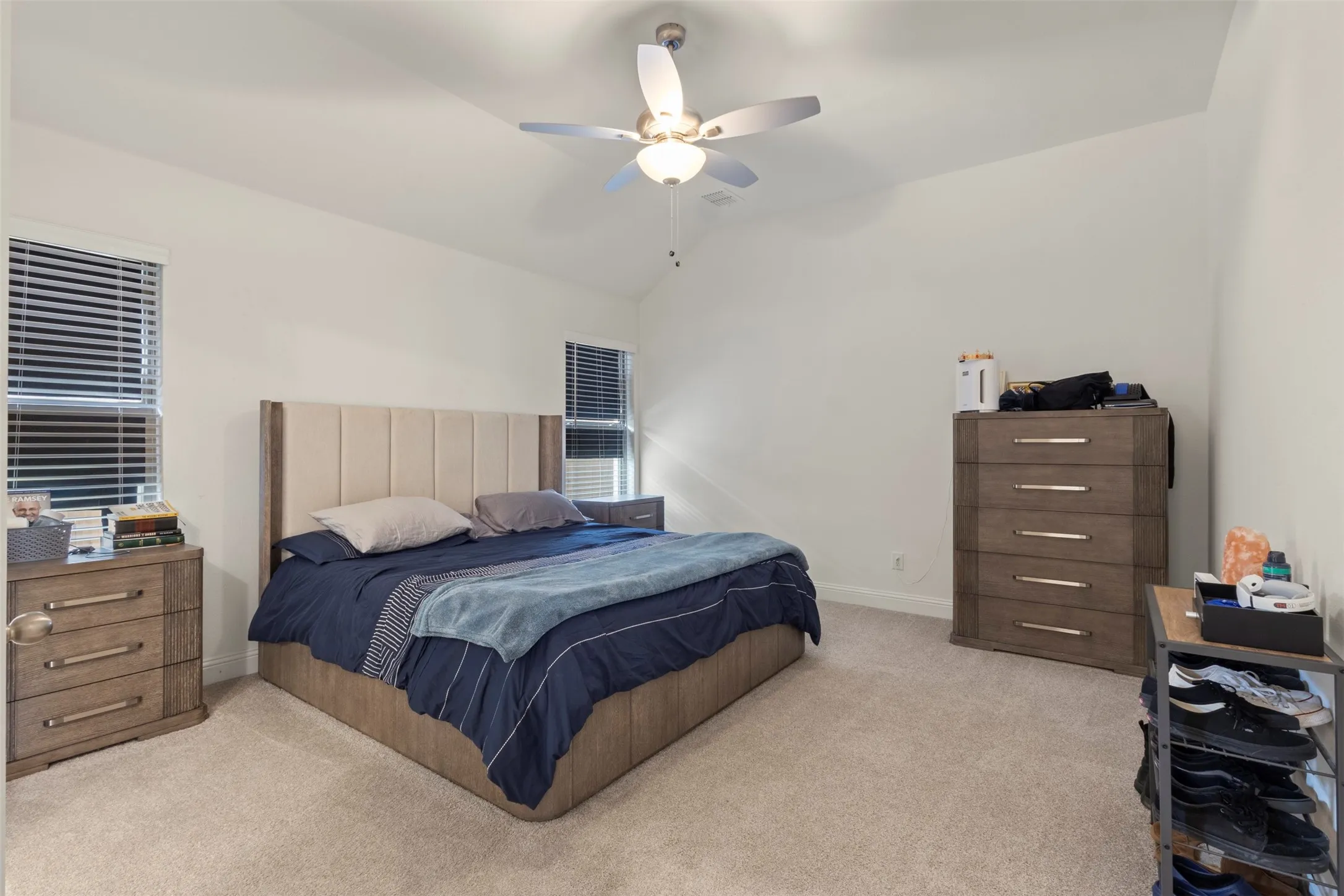 Vaulted ceiling with a ceiling fan light fixture, two windows with blinds, and neutral carpeting