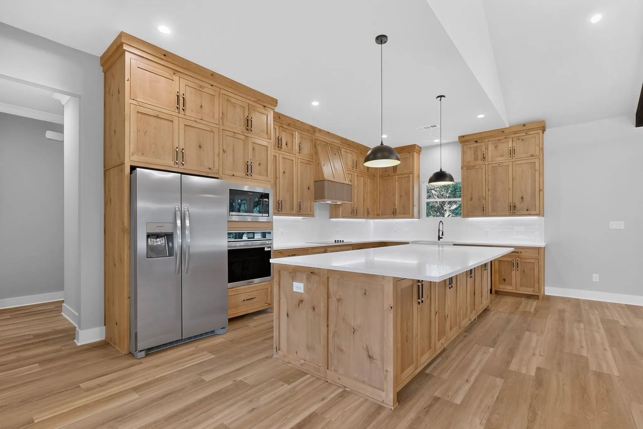 Spacious kitchen featuring custom wood cabinetry, white quartz countertops, stainless steel side-by-side refrigerator, and a large center island with seating