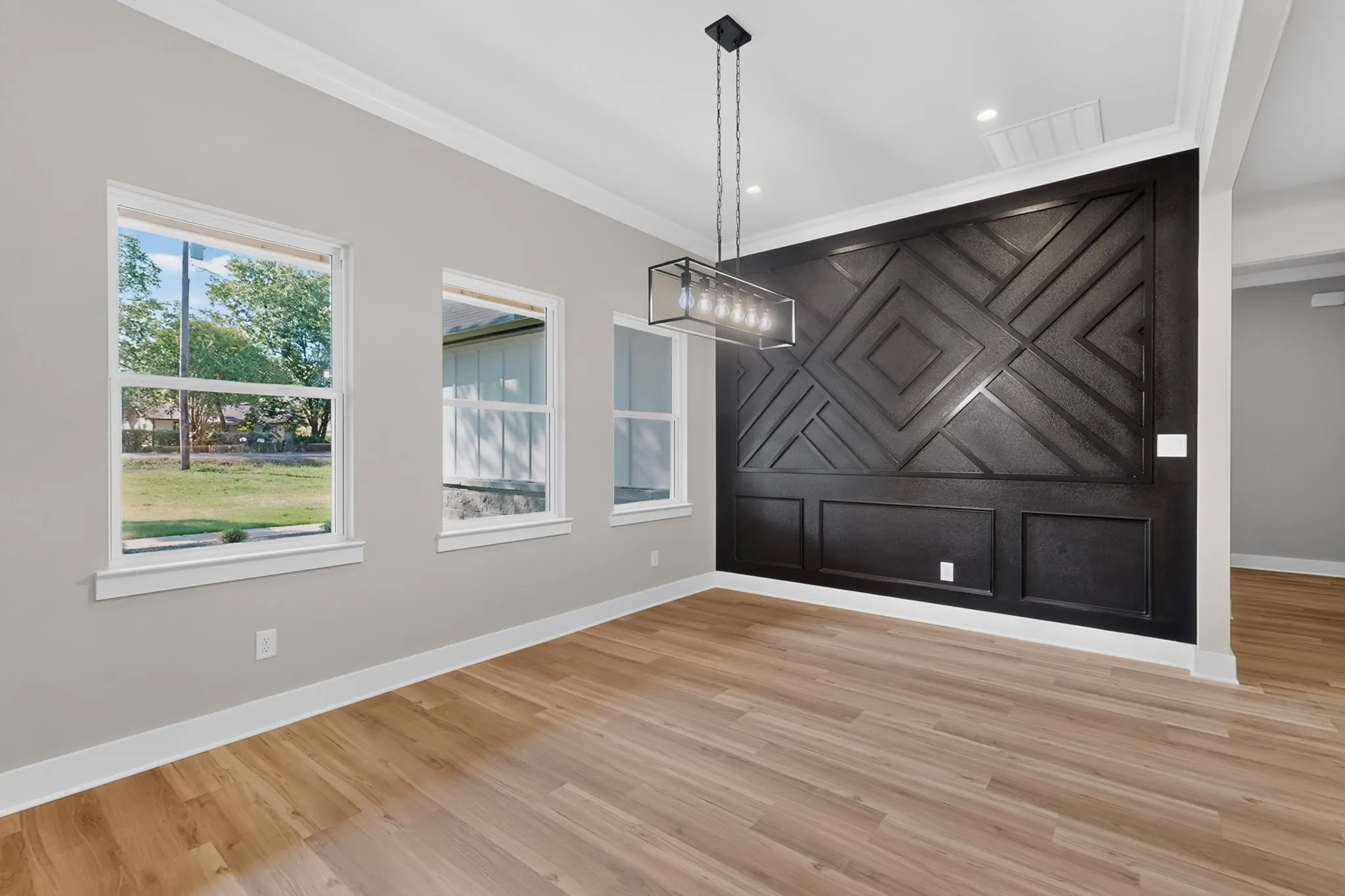 Wood-finish flooring, accent wall with geometric paneling, contemporary linear chandelier, recessed lighting, and crown molding