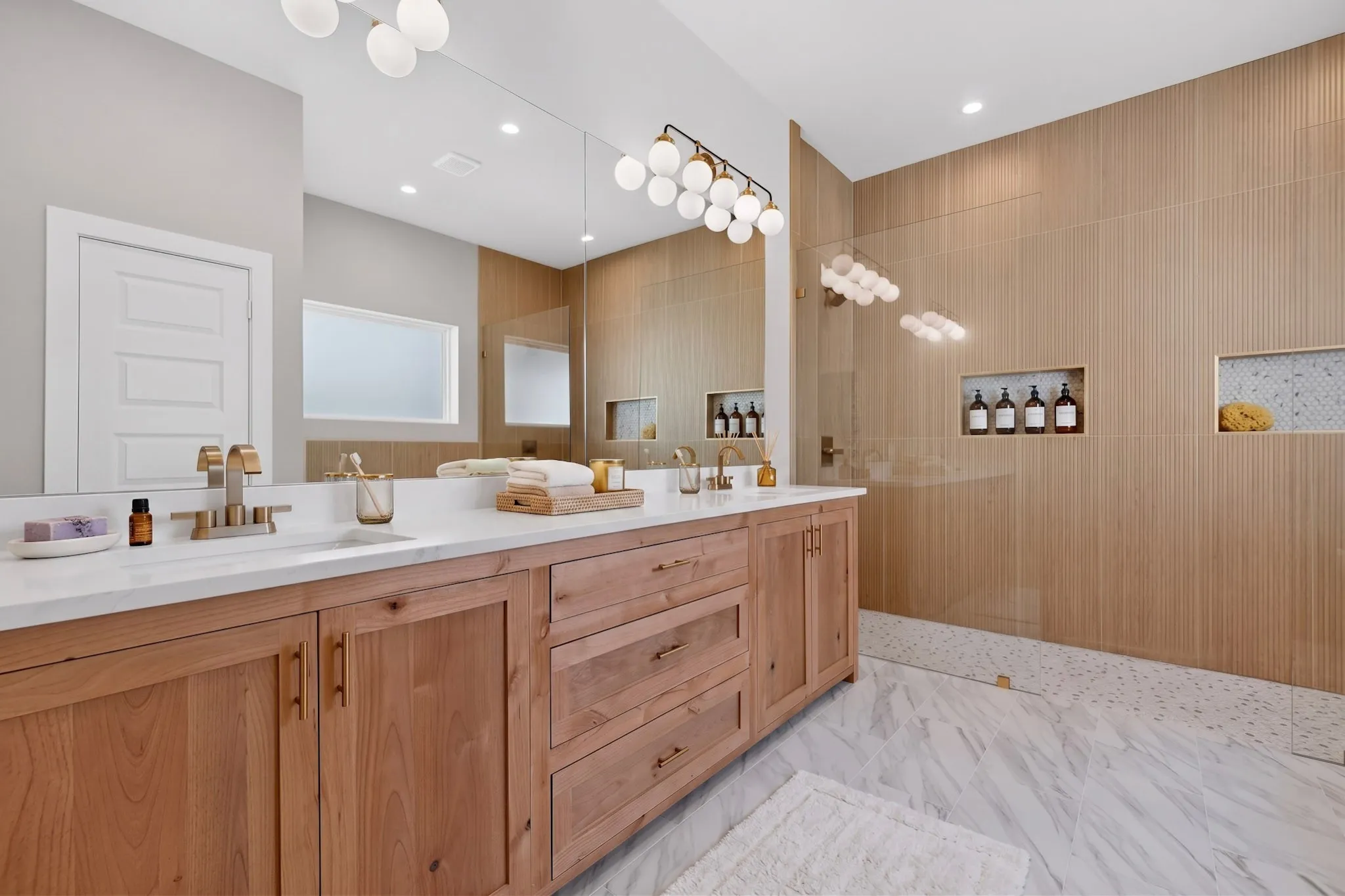Dual vanity with white countertop, brass fixtures, wood-finish cabinetry, and full-wall mirror