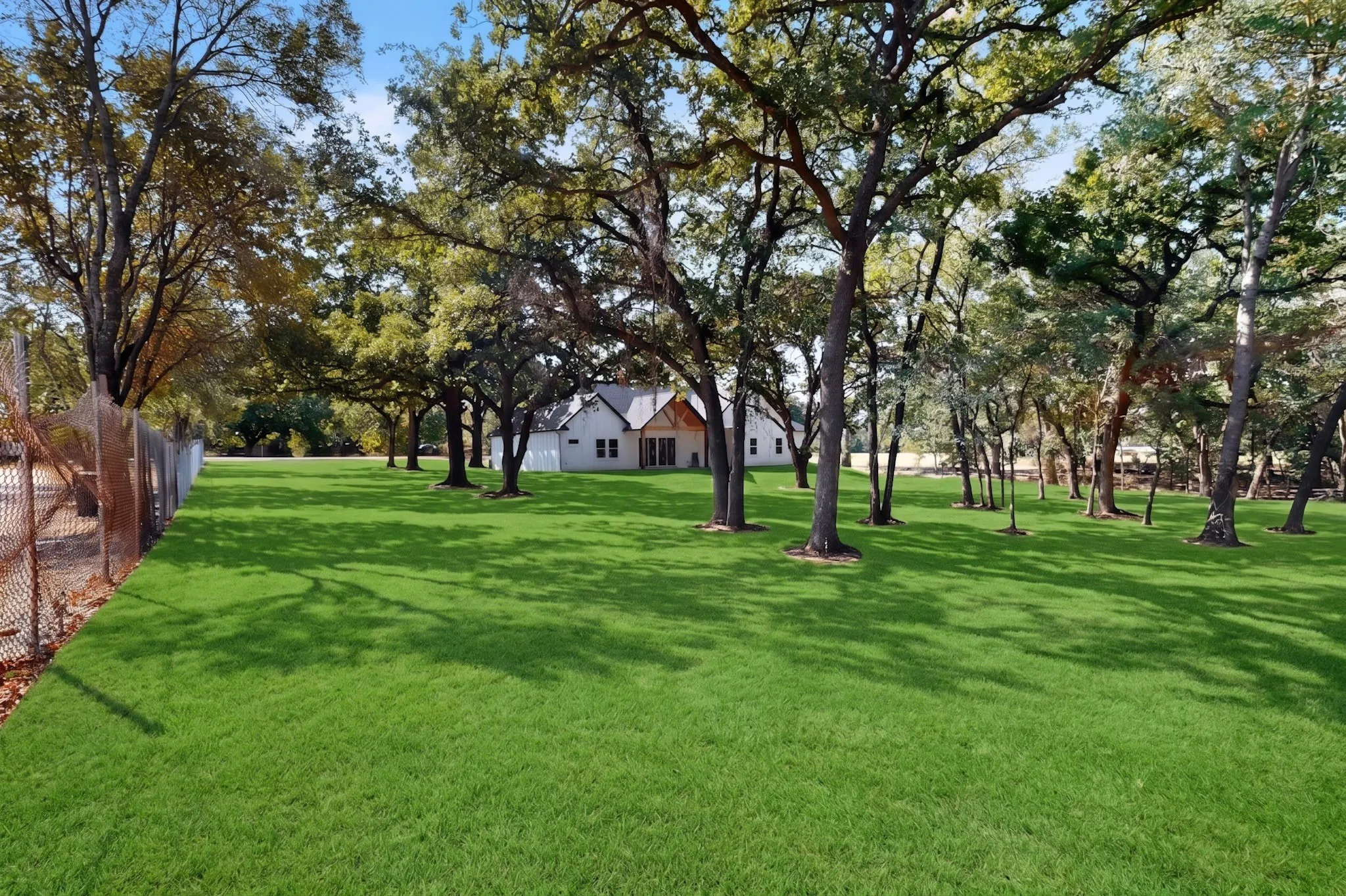Expansive grassy lawn surrounded by mature trees, featuring a white exterior residence with a contrasting roof and wood elements