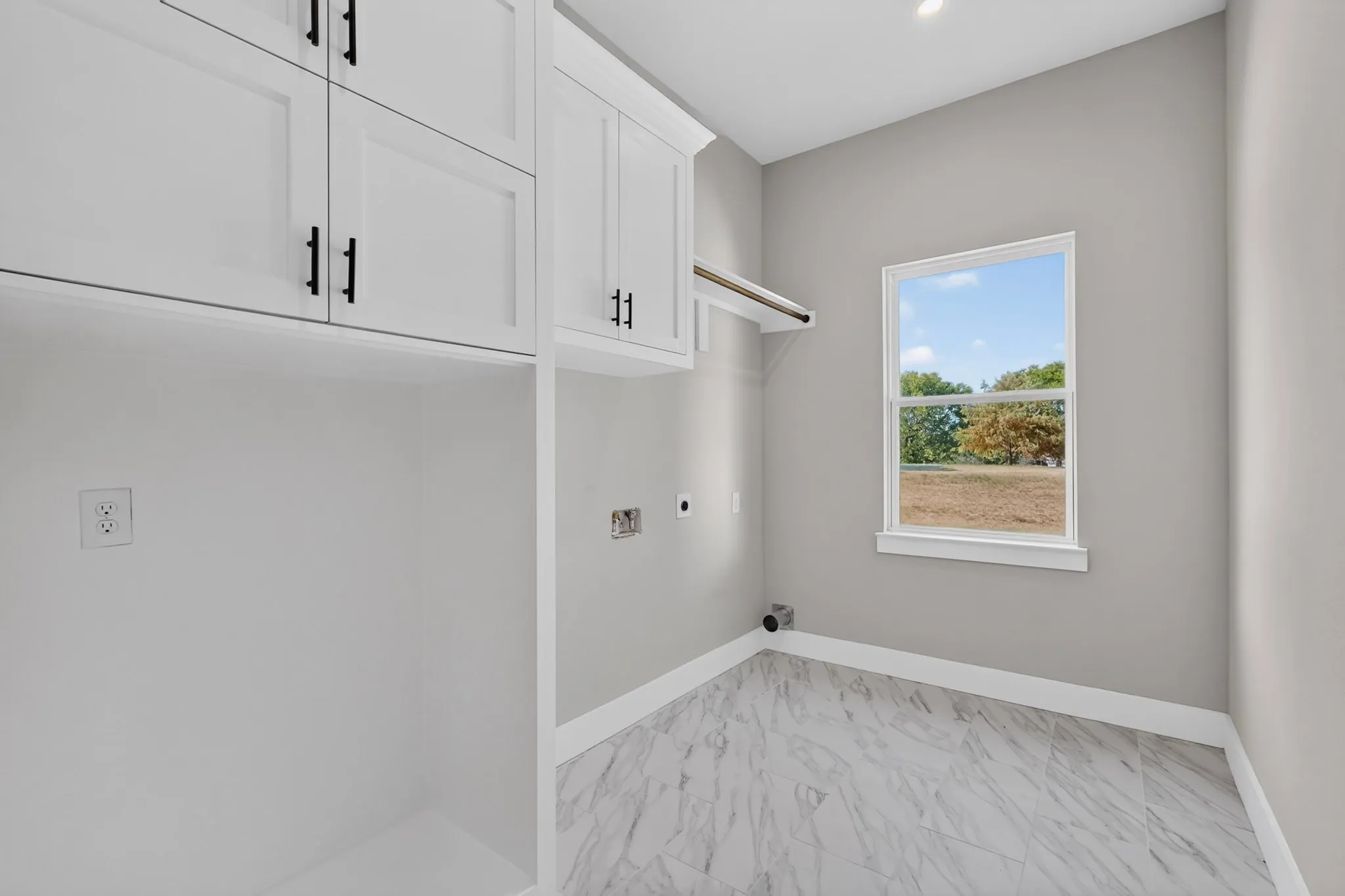 White shaker-style cabinetry with matte black hardware, built-in shelving, a single window, and light-toned tile flooring