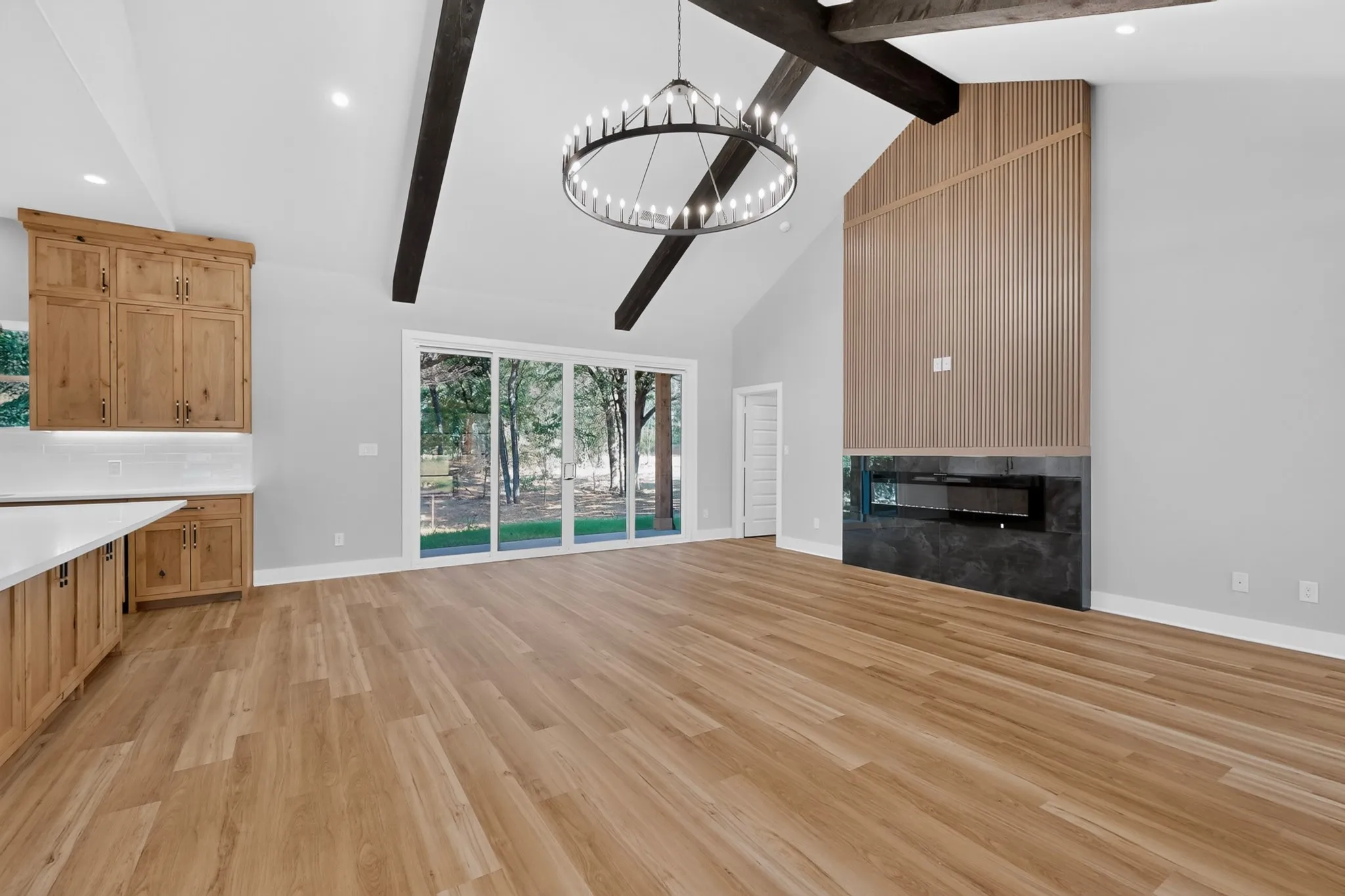 Vaulted ceiling with exposed wood beams, wood-finish flooring, built-in electric fireplace with stone surround, wall of sliding glass doors, and a built-in cabinetry system